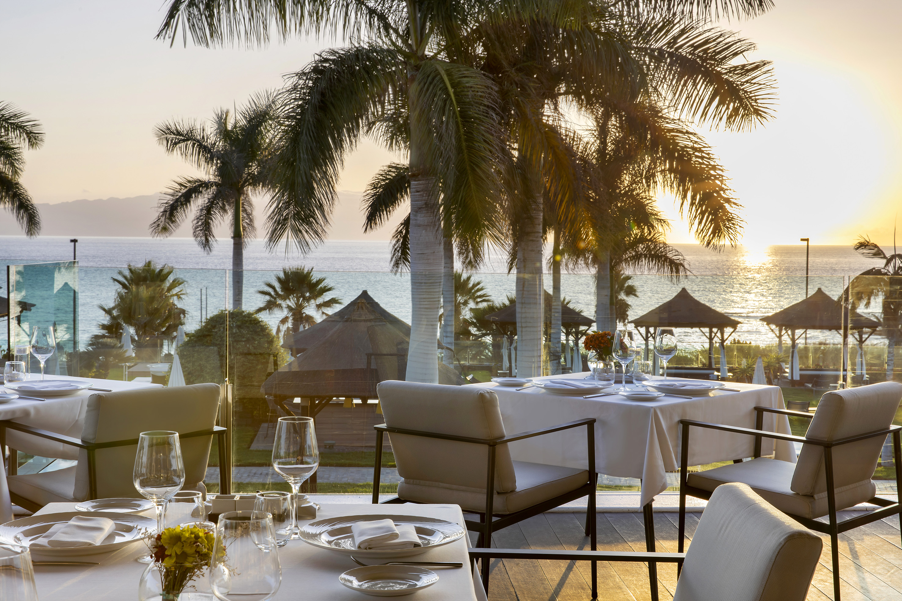 Elegant beachfront restaurant with palm trees, ocean view, and sunset.