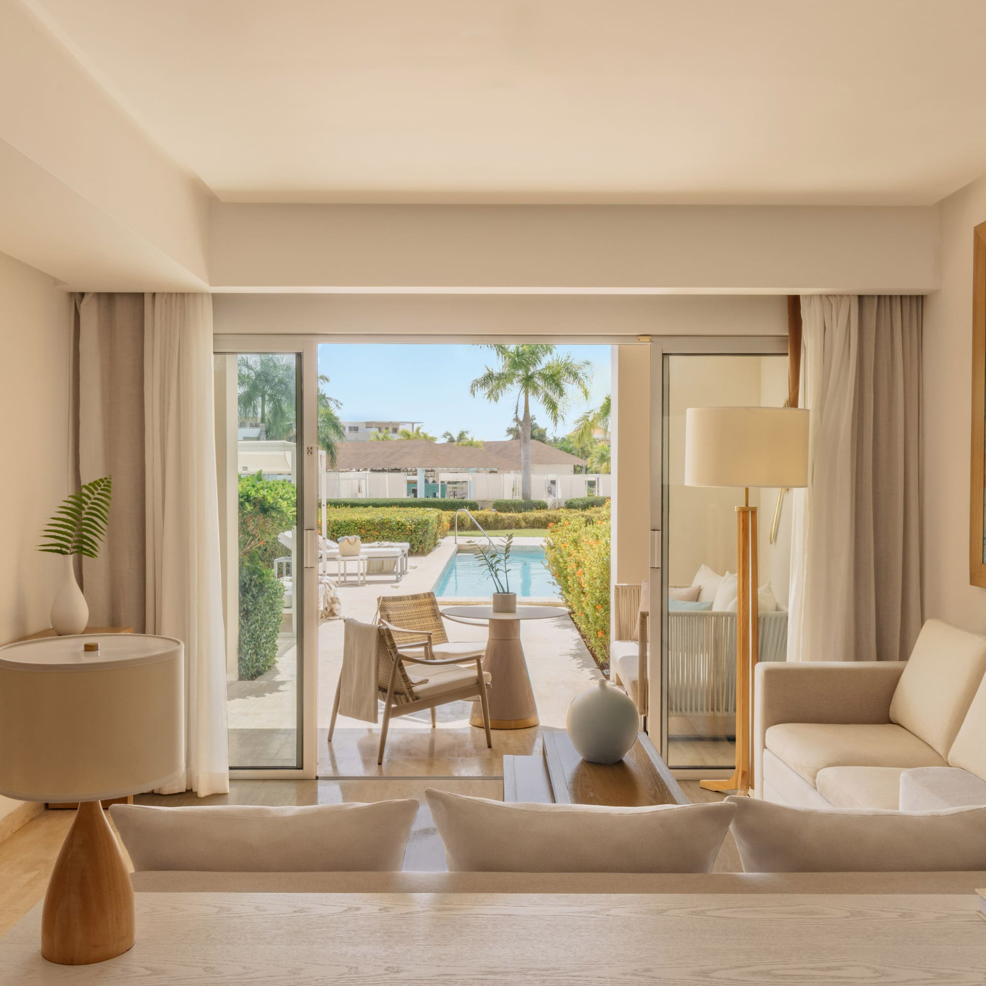 Bright hotel suite living room opening to private pool patio with palm trees.