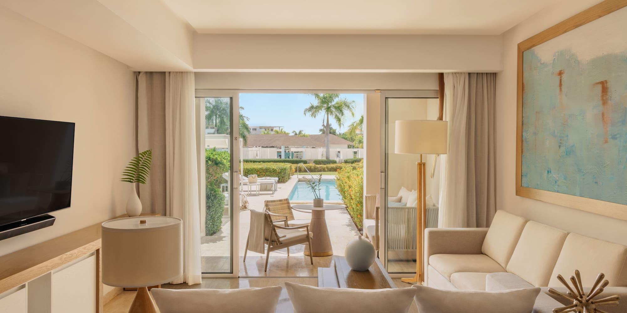 Bright hotel suite living room opening to private pool patio with palm trees.