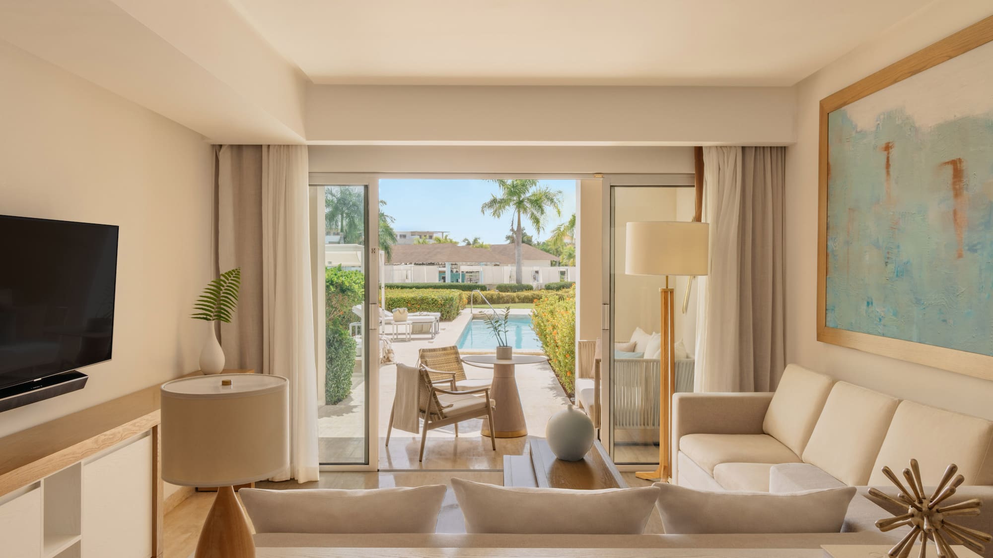 Bright hotel suite living room opening to private pool patio with palm trees.