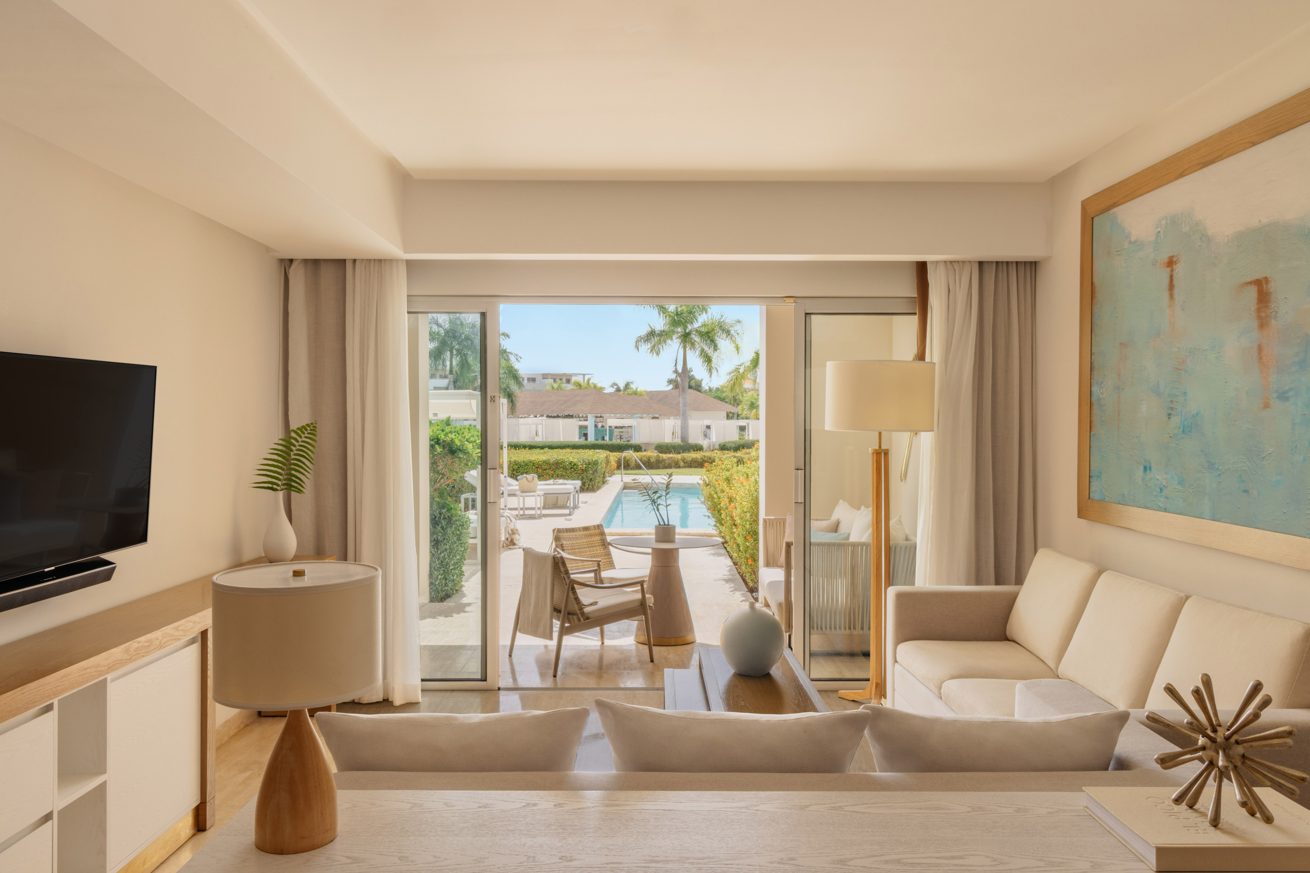 Bright hotel suite living room opening to private pool patio with palm trees.