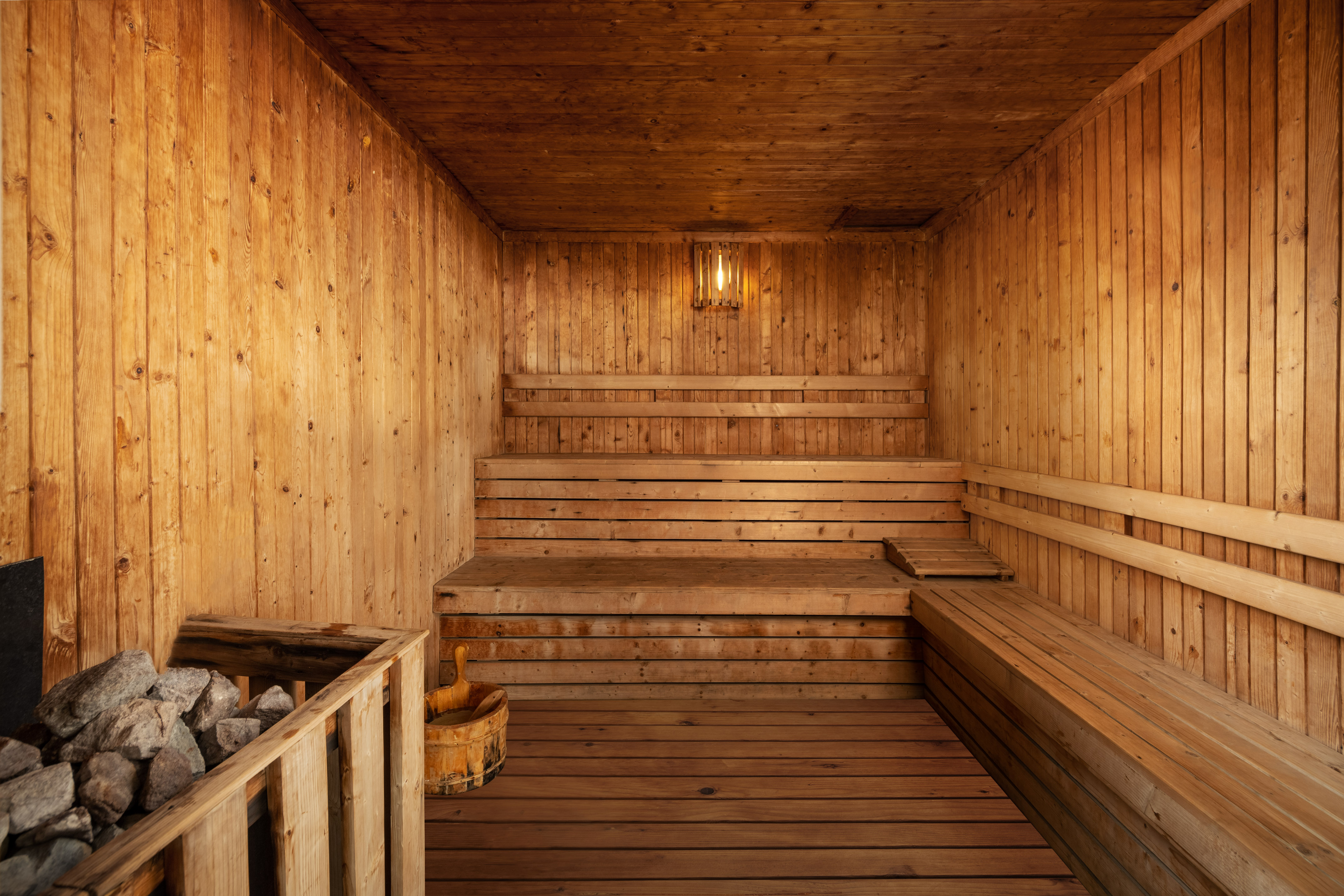 Traditional wooden sauna interior with tiered benches, heater, and warm light.