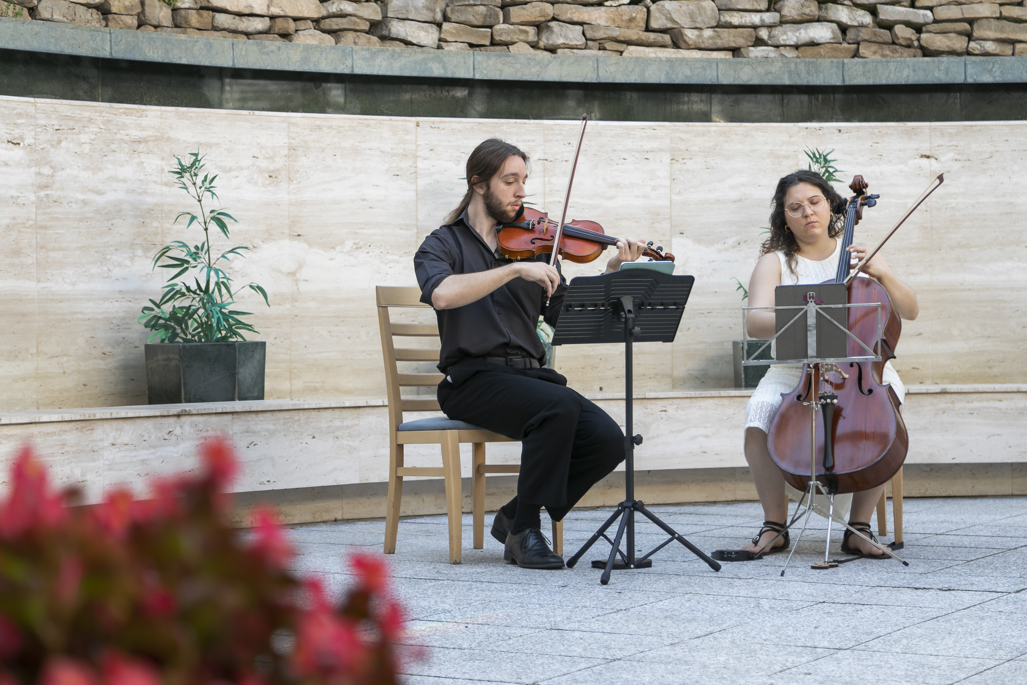 Violinist and cellist perform classical music outdoors.