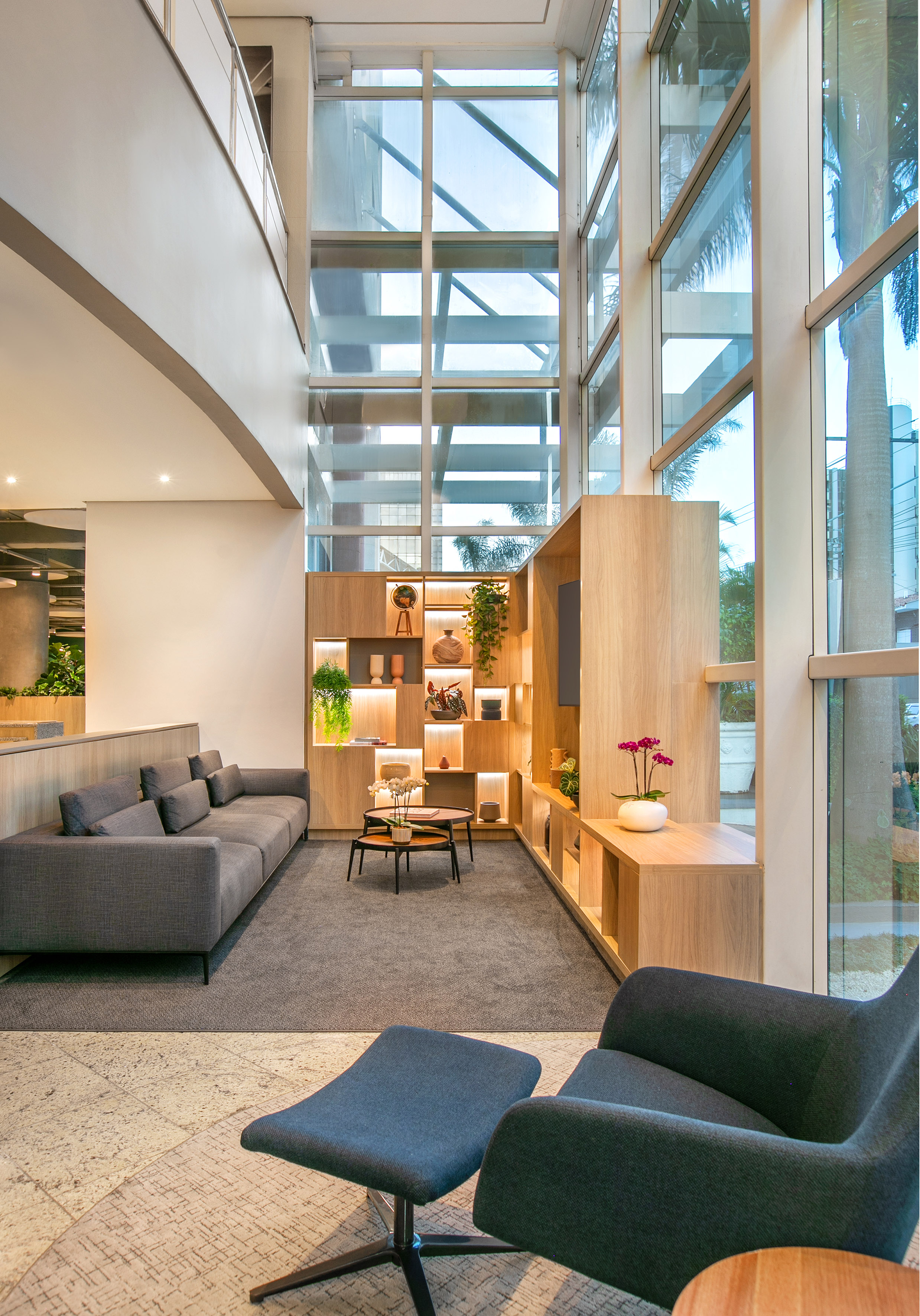 Modern lobby with grey seating, illuminated wooden shelves, and large windows.