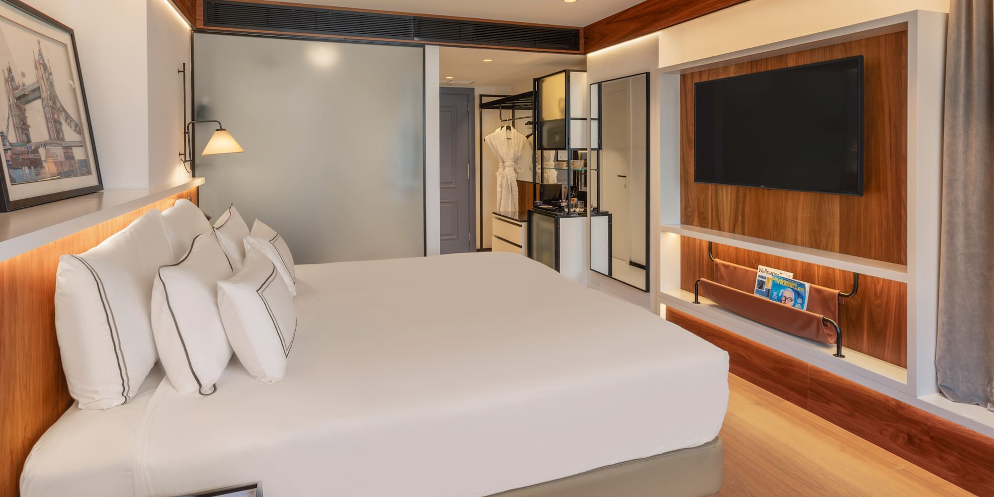 Modern hotel bedroom with white bed, wall-mounted TV, and elegant wood decor.