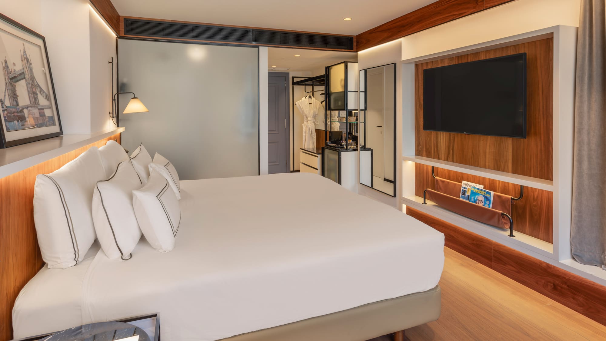 Modern hotel bedroom with white bed, wall-mounted TV, and elegant wood decor.