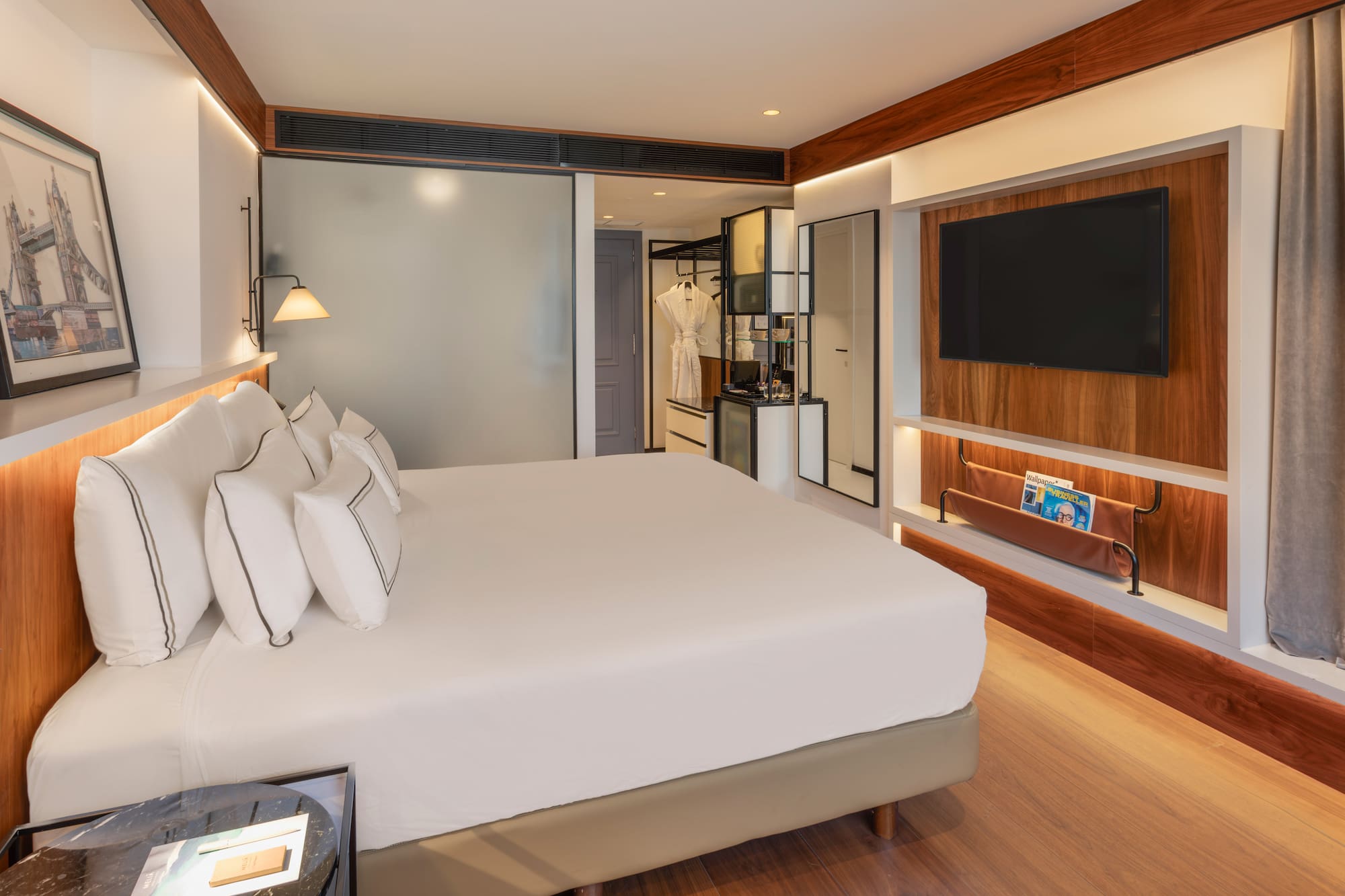 Modern hotel bedroom with white bed, wall-mounted TV, and elegant wood decor.