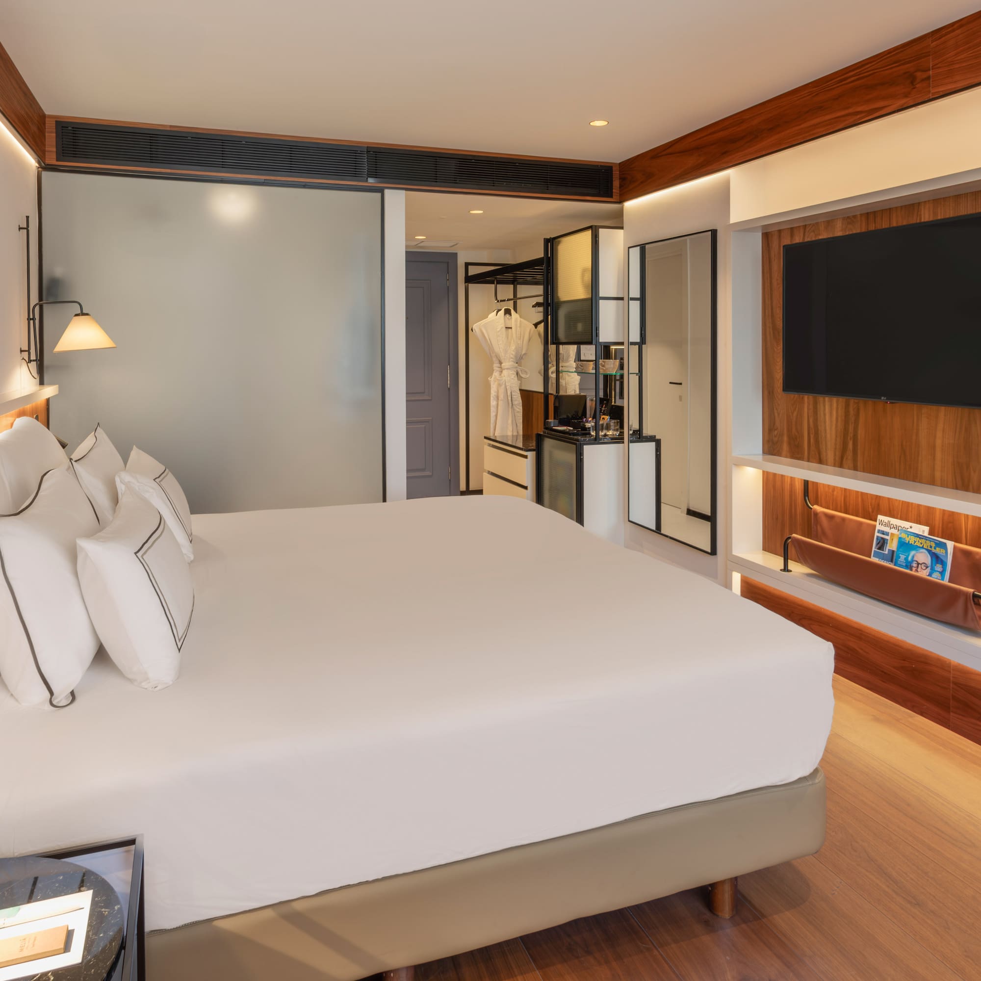 Modern hotel bedroom with white bed, wall-mounted TV, and elegant wood decor.
