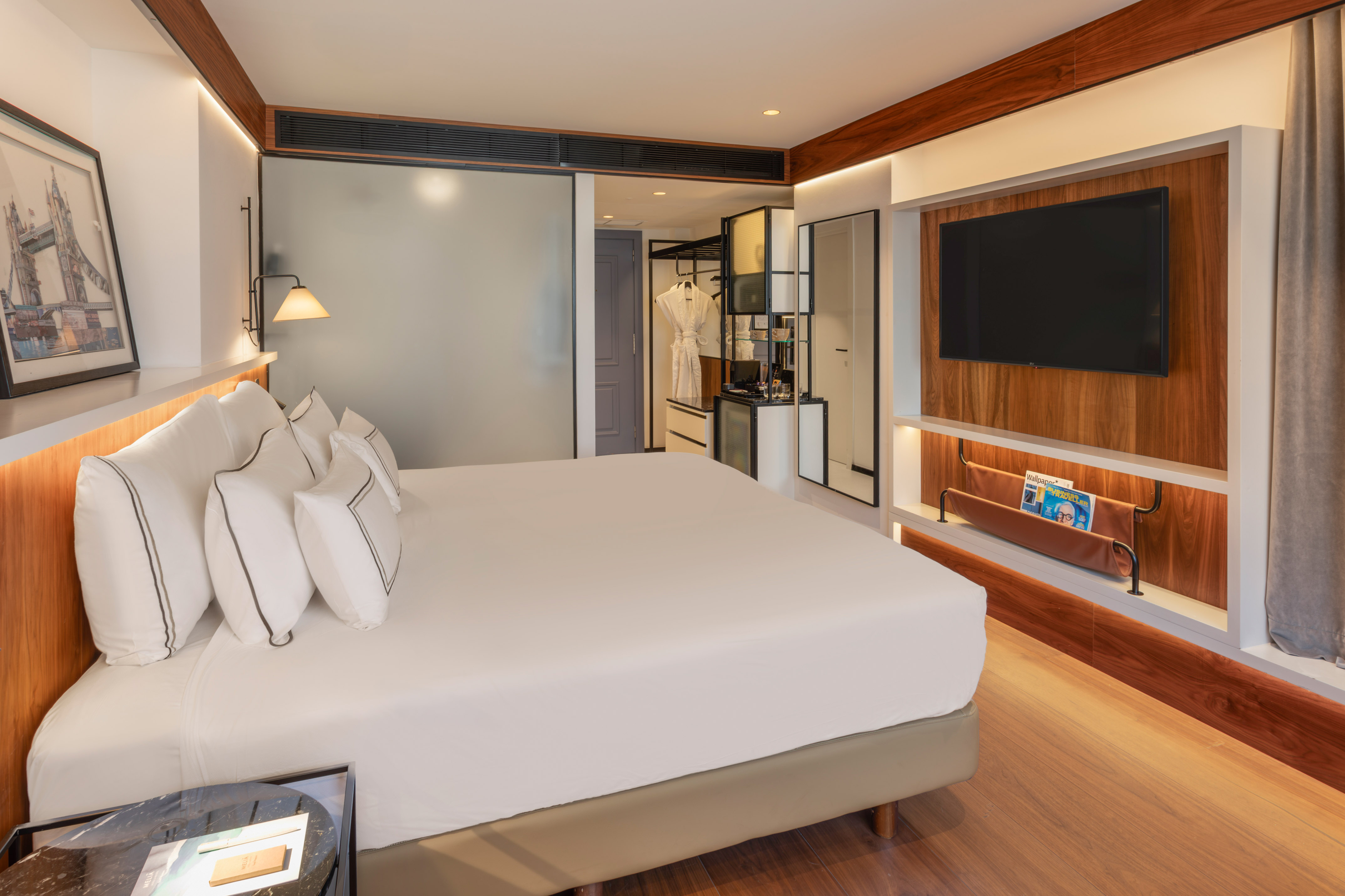 Modern hotel bedroom with white bed, wall-mounted TV, and elegant wood decor.