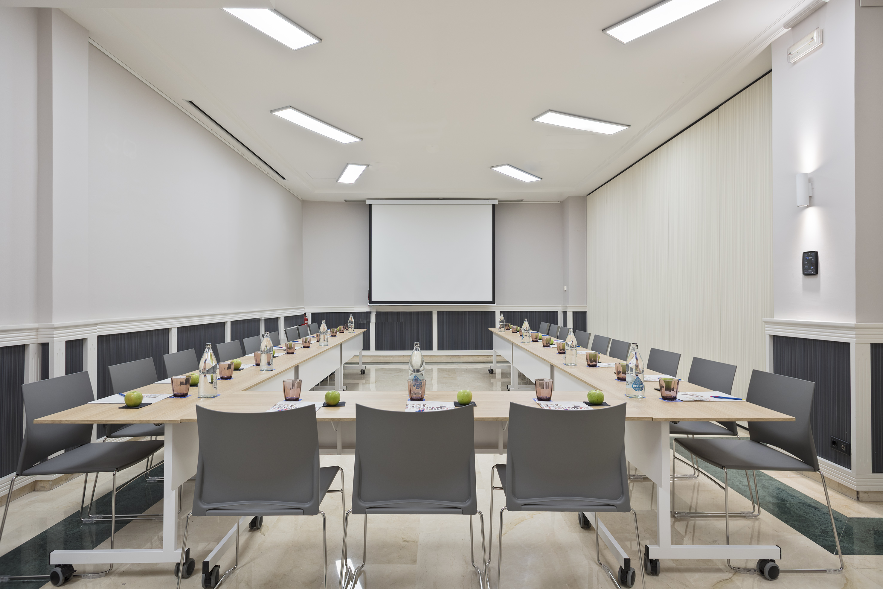 Modern U-shaped conference room with projector screen and grey chairs.