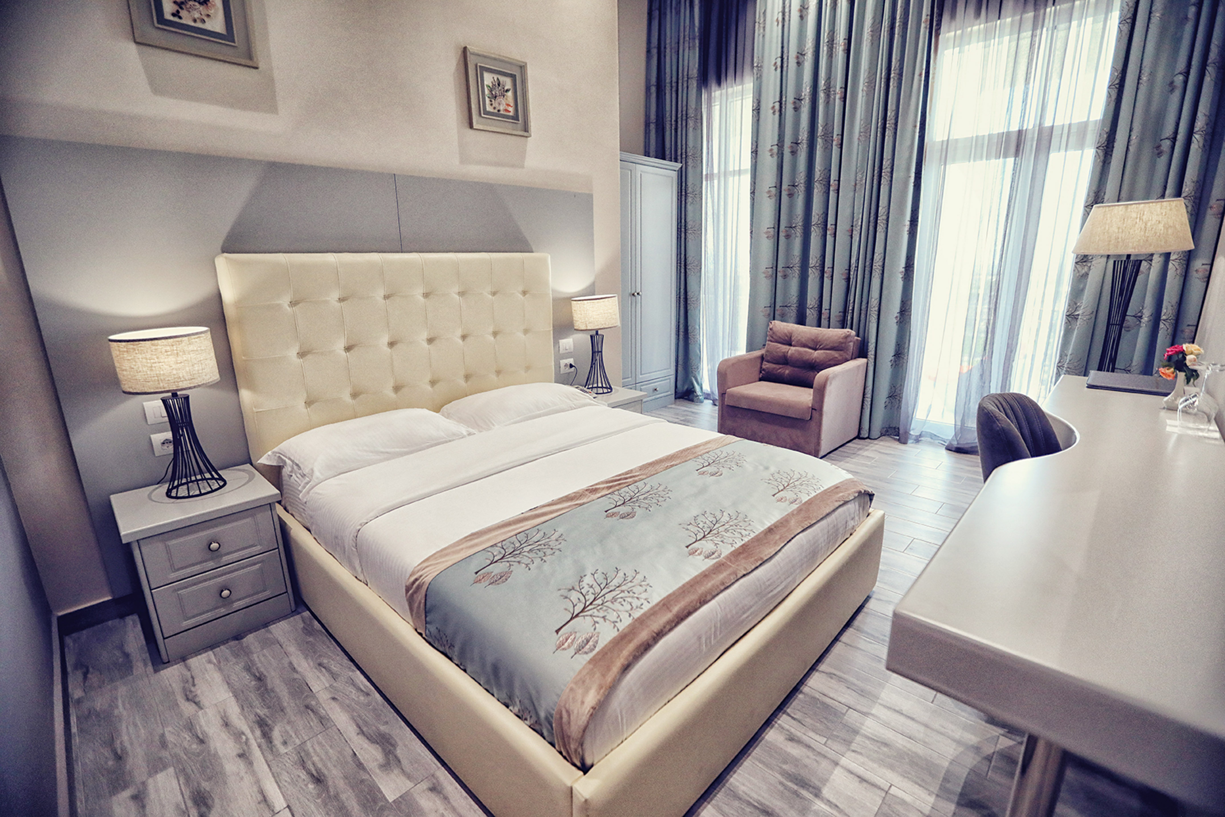 Elegant hotel bedroom with tufted king bed, desk, and patterned curtains.