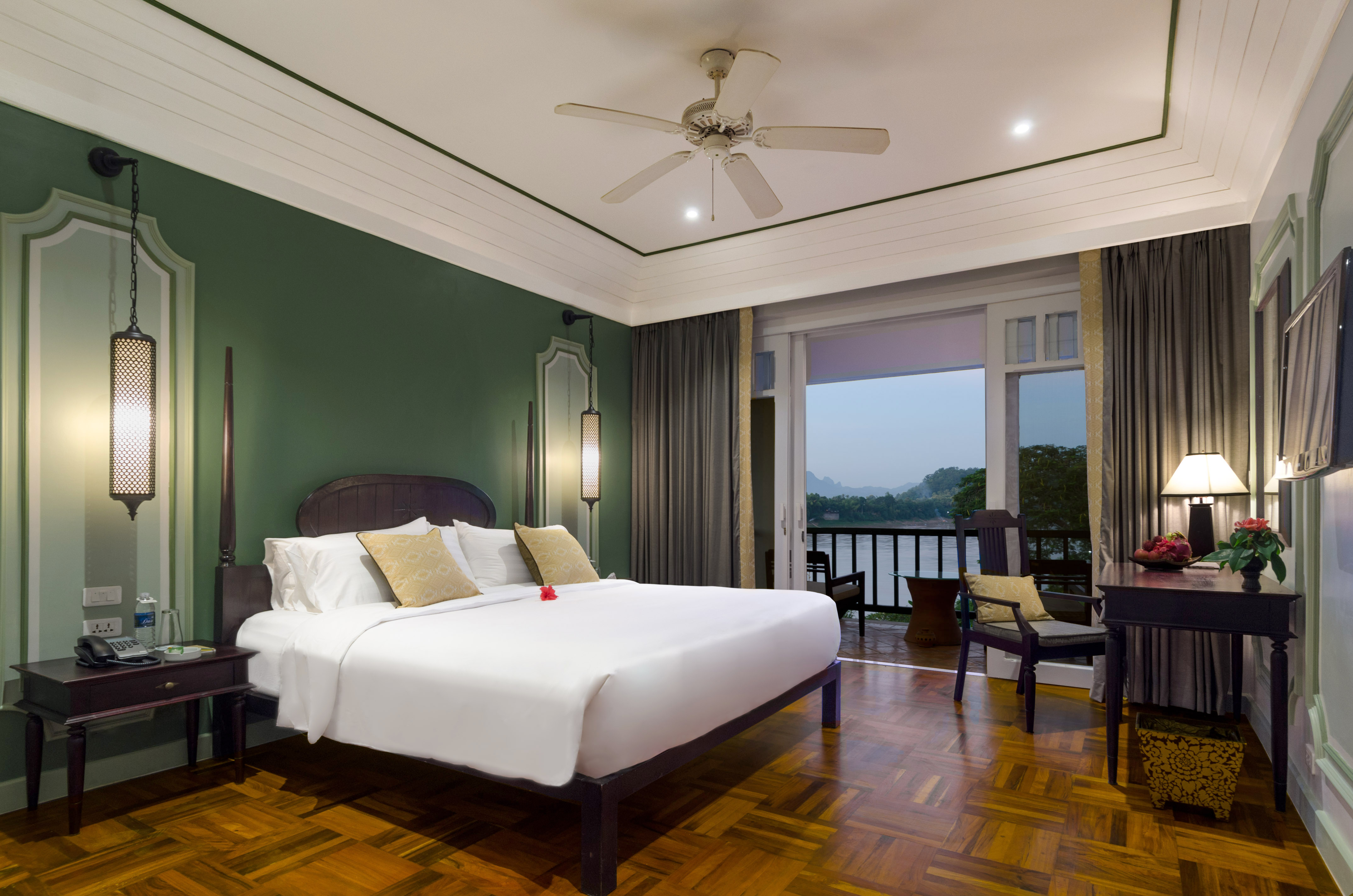 Luxury hotel room with green walls, wood floor, and river view balcony.