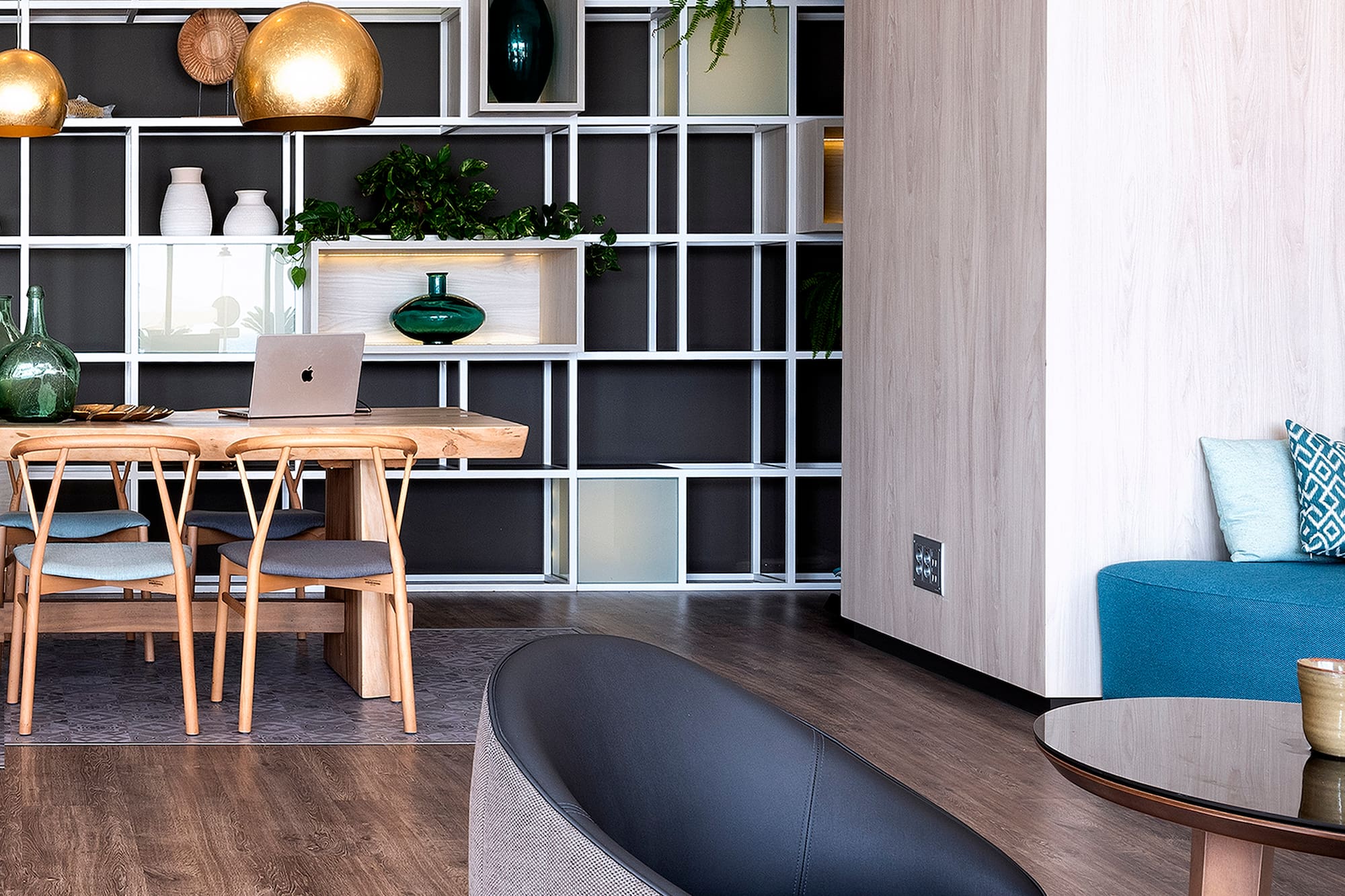 Modern dining and lounge space with wooden table, plant-decorated shelves.