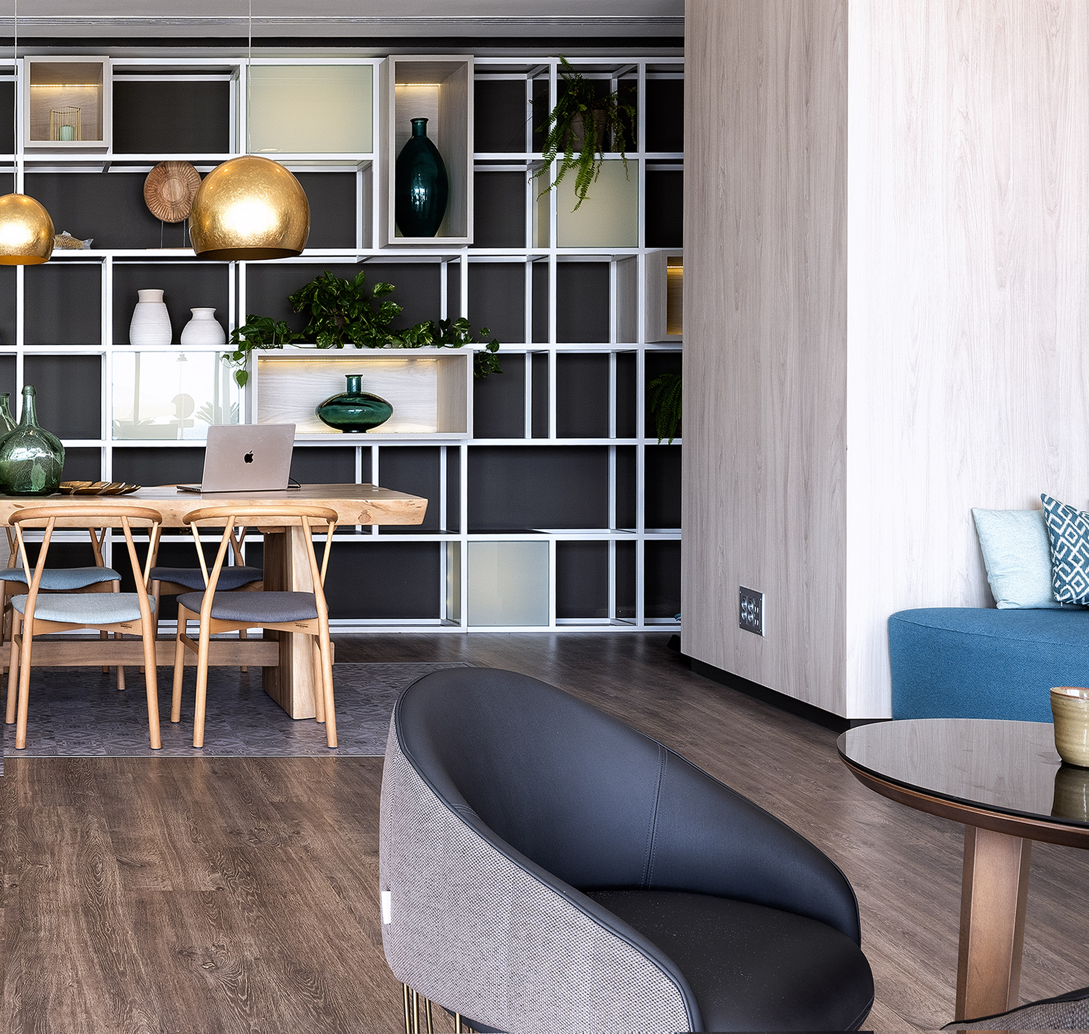 Modern dining and lounge space with wooden table, plant-decorated shelves.