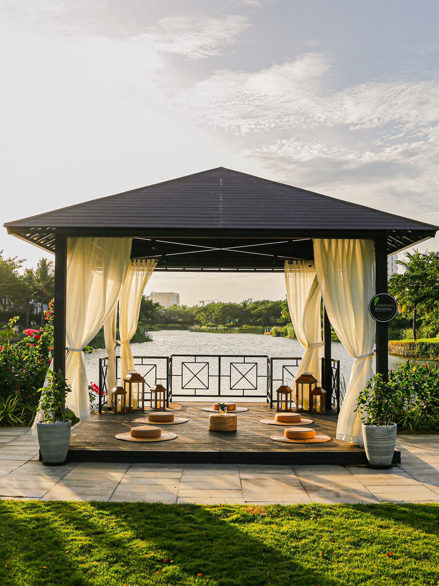a gazebo with white curtains and a pond in the background