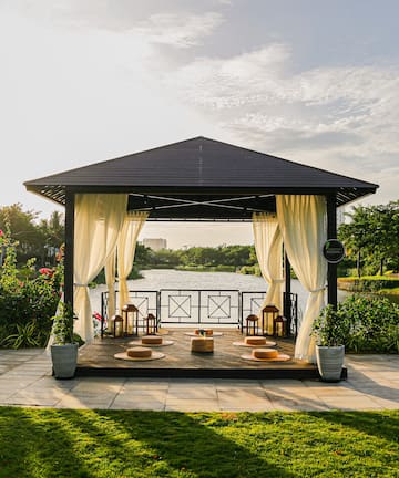 a gazebo with white curtains and a pond in the background