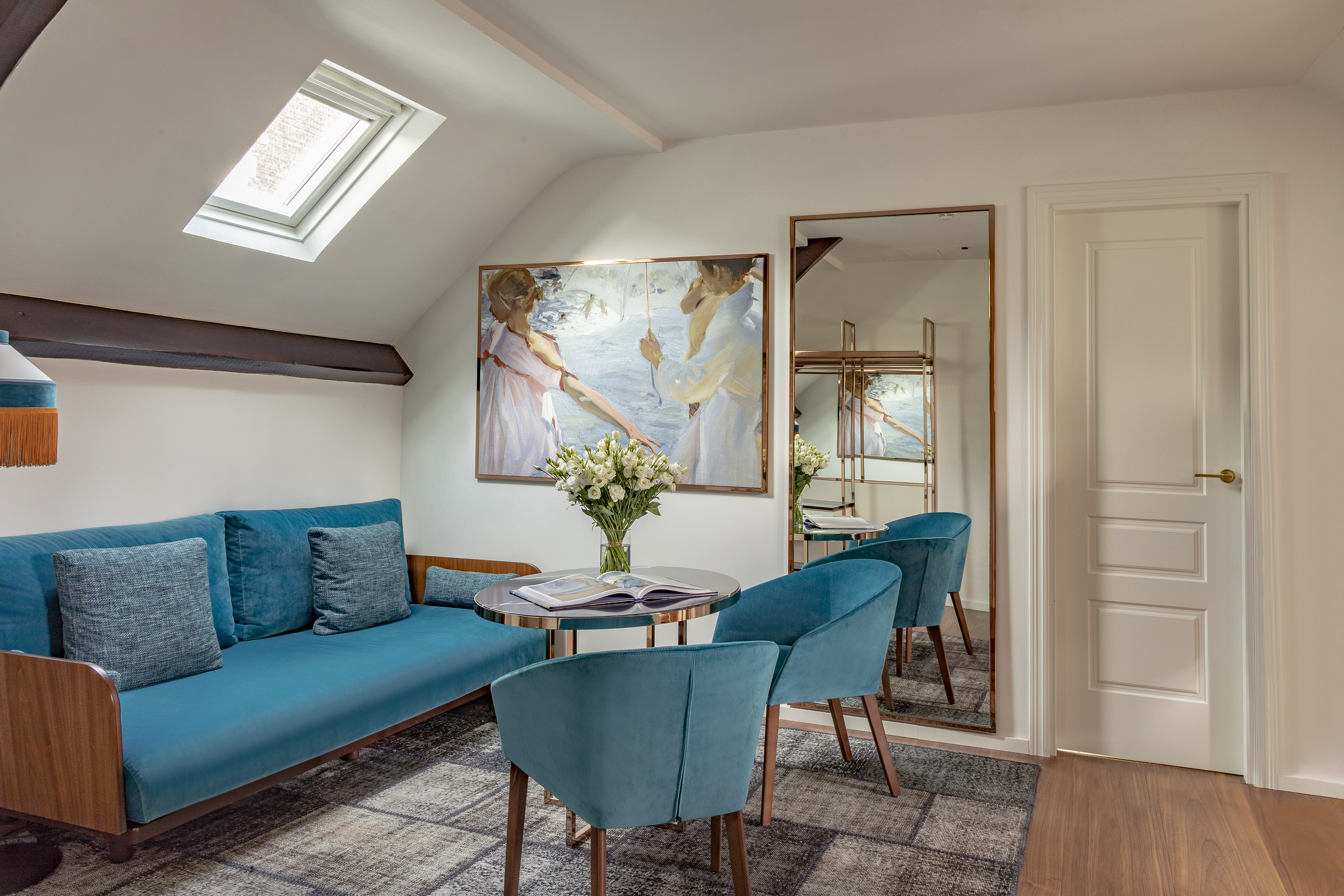 Attic living room with teal velvet sofa, skylight, mirror, and large painting.