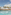 Modern resort hotel, blue pool, palm trees, and thatched cabanas under sunny sky.