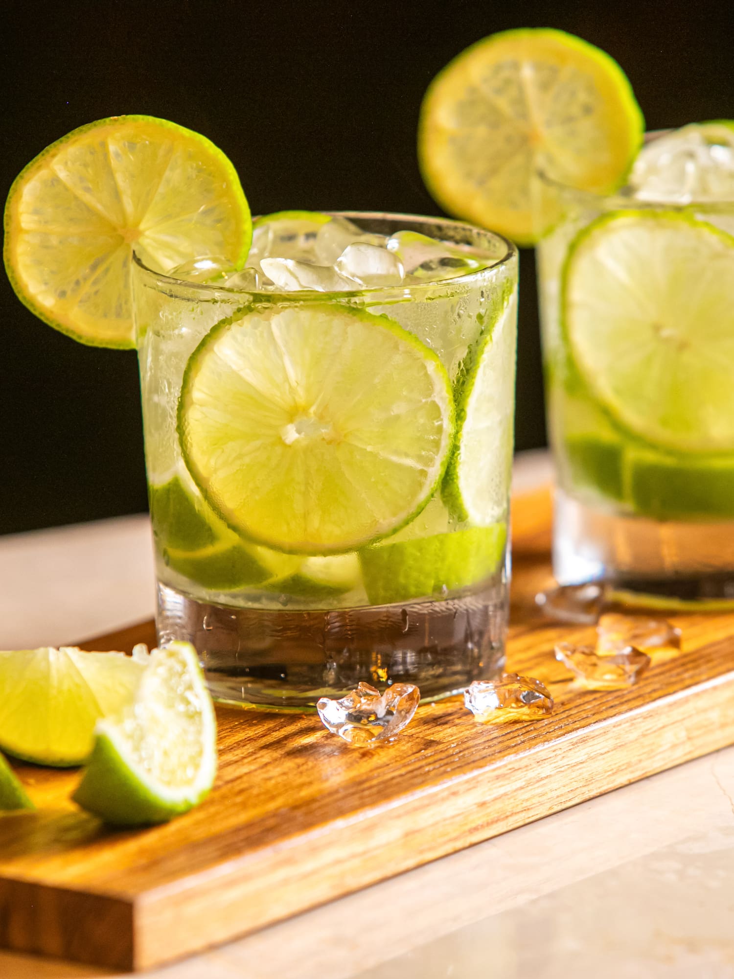 Two refreshing lime cocktails with ice and lime slices on a wooden tray.