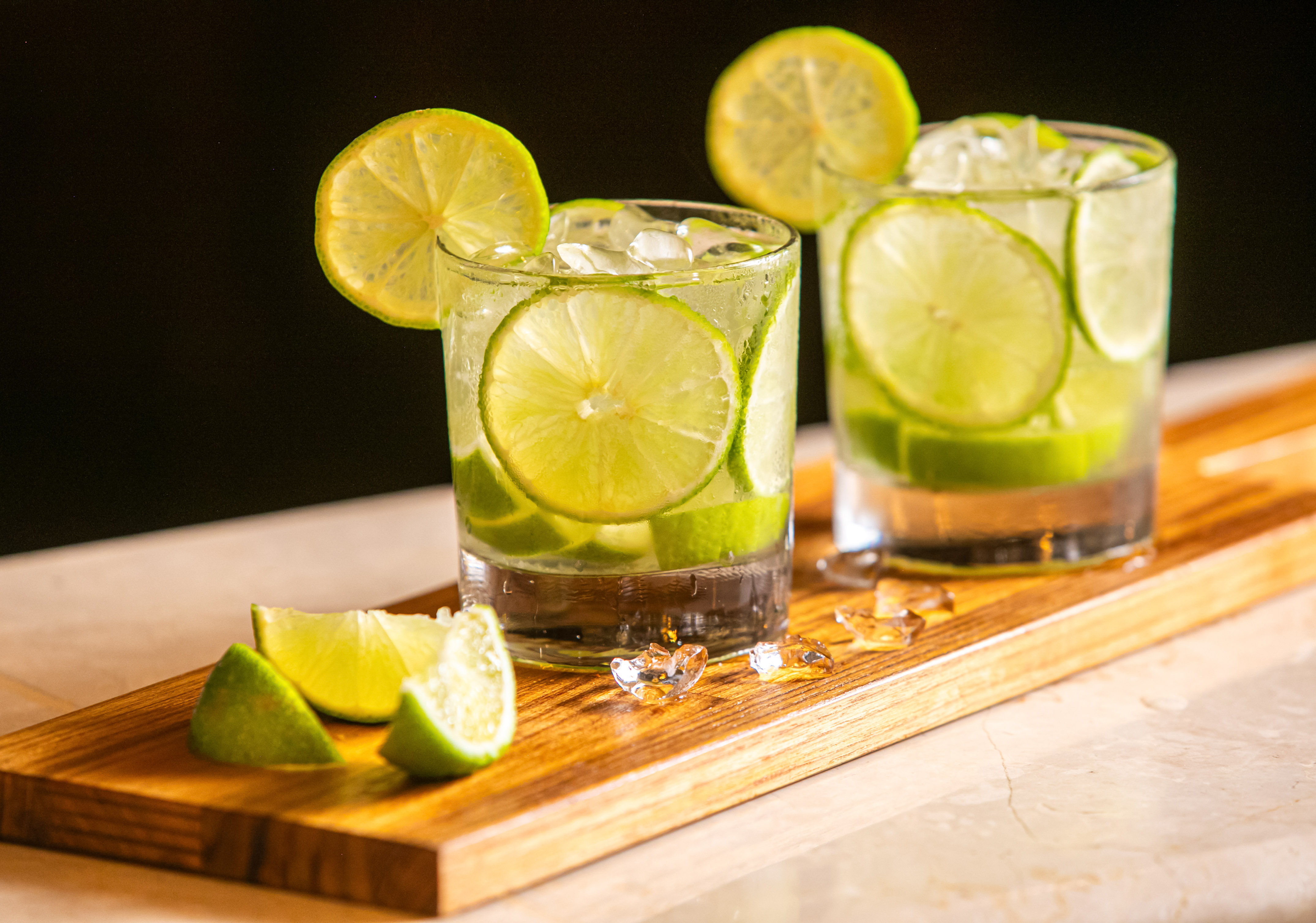 Two refreshing lime cocktails with ice and lime slices on a wooden tray.