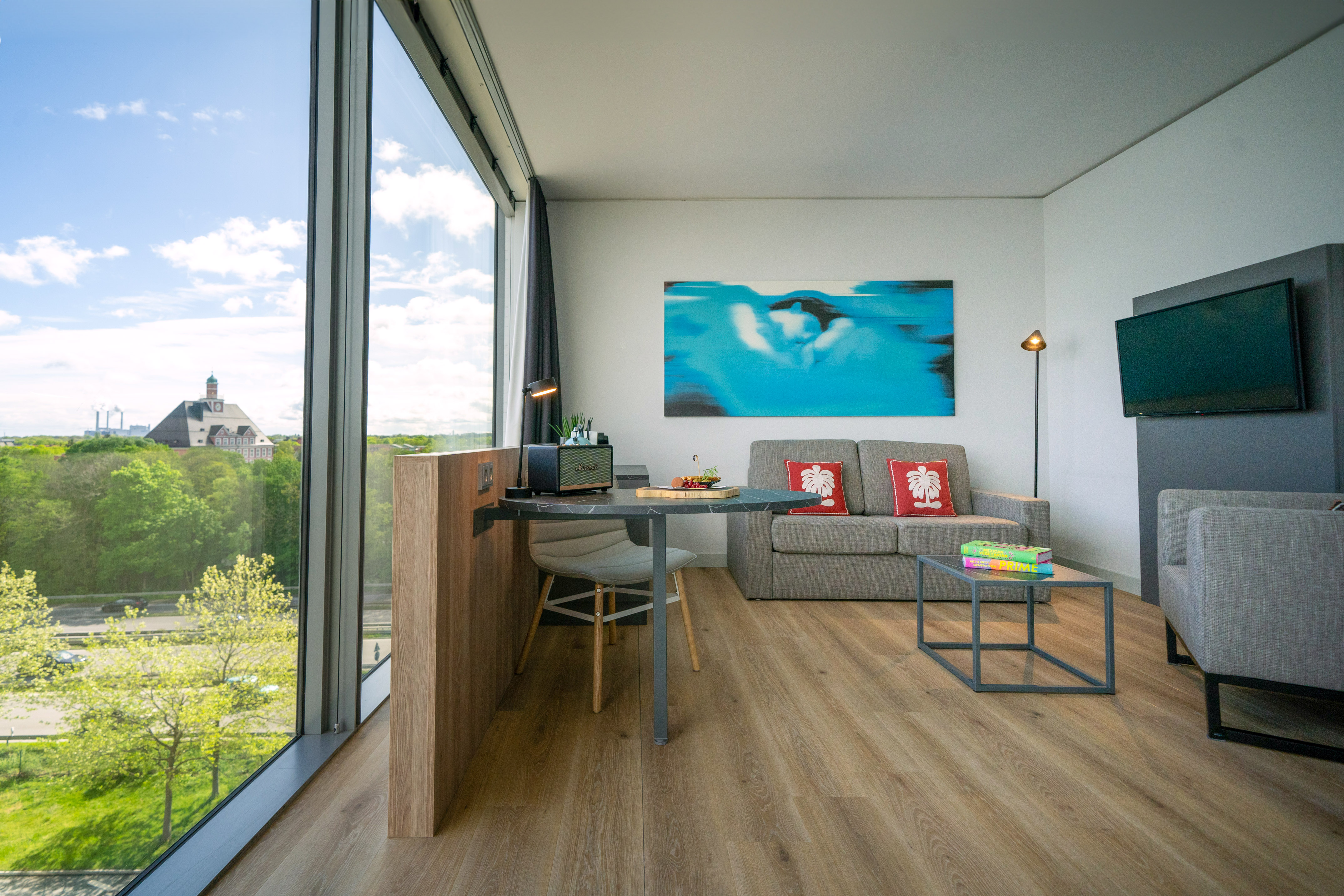Modern hotel room with panoramic city view, sofa, and dining table.