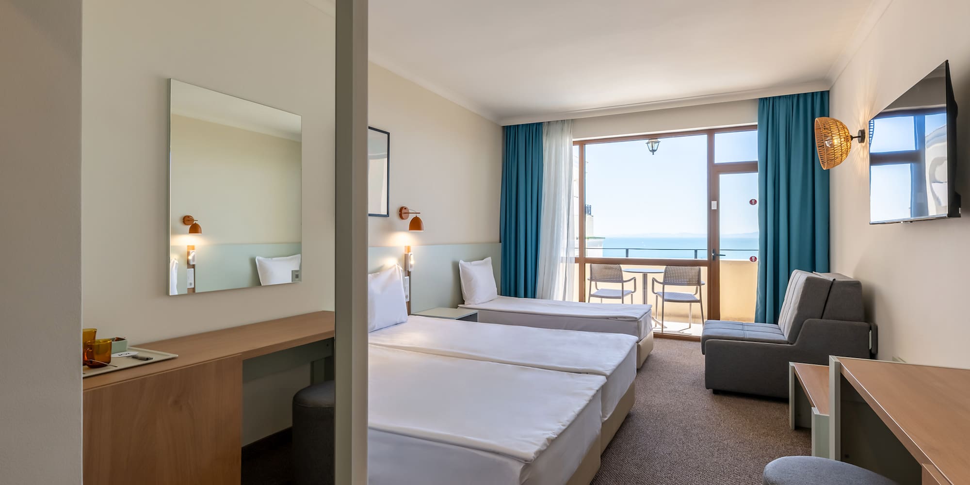 Hotel room with twin beds, desk, and balcony with ocean view.