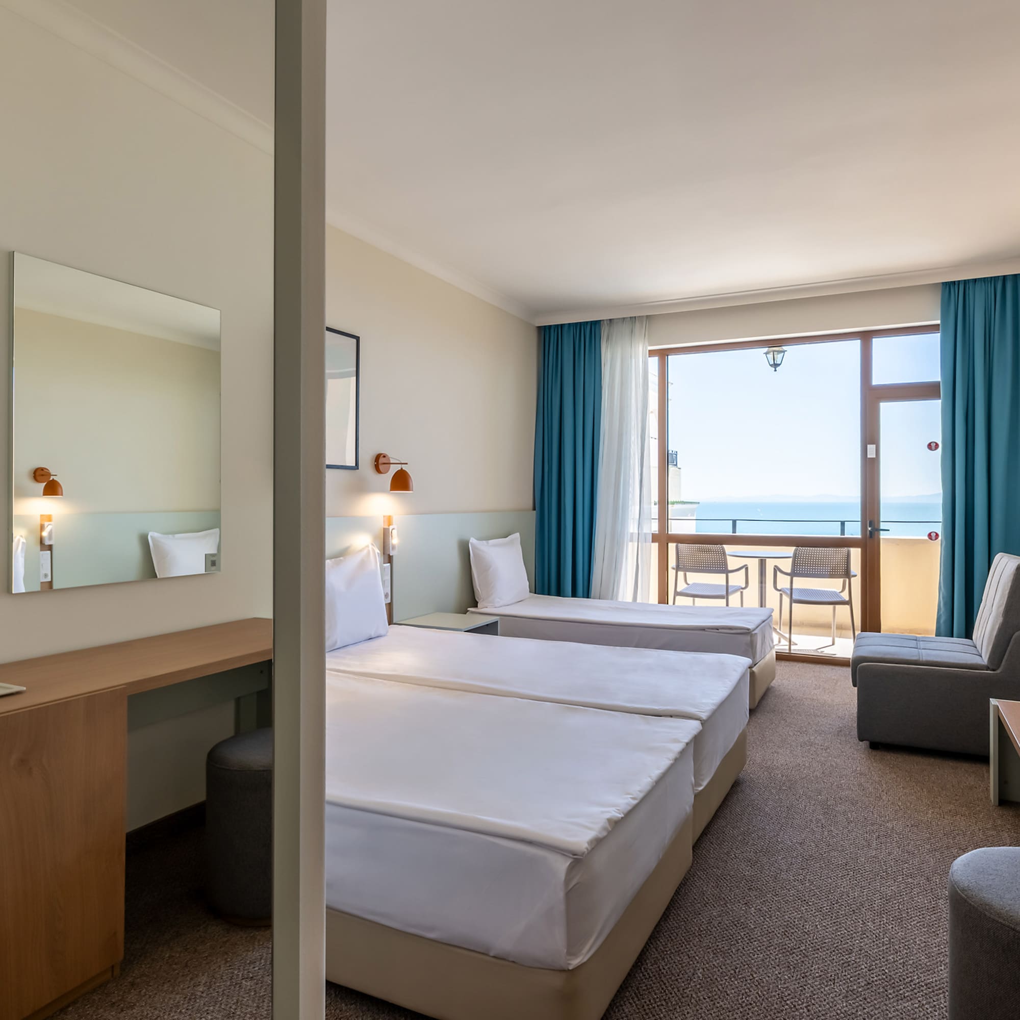 Hotel room with twin beds, desk, and balcony with ocean view.
