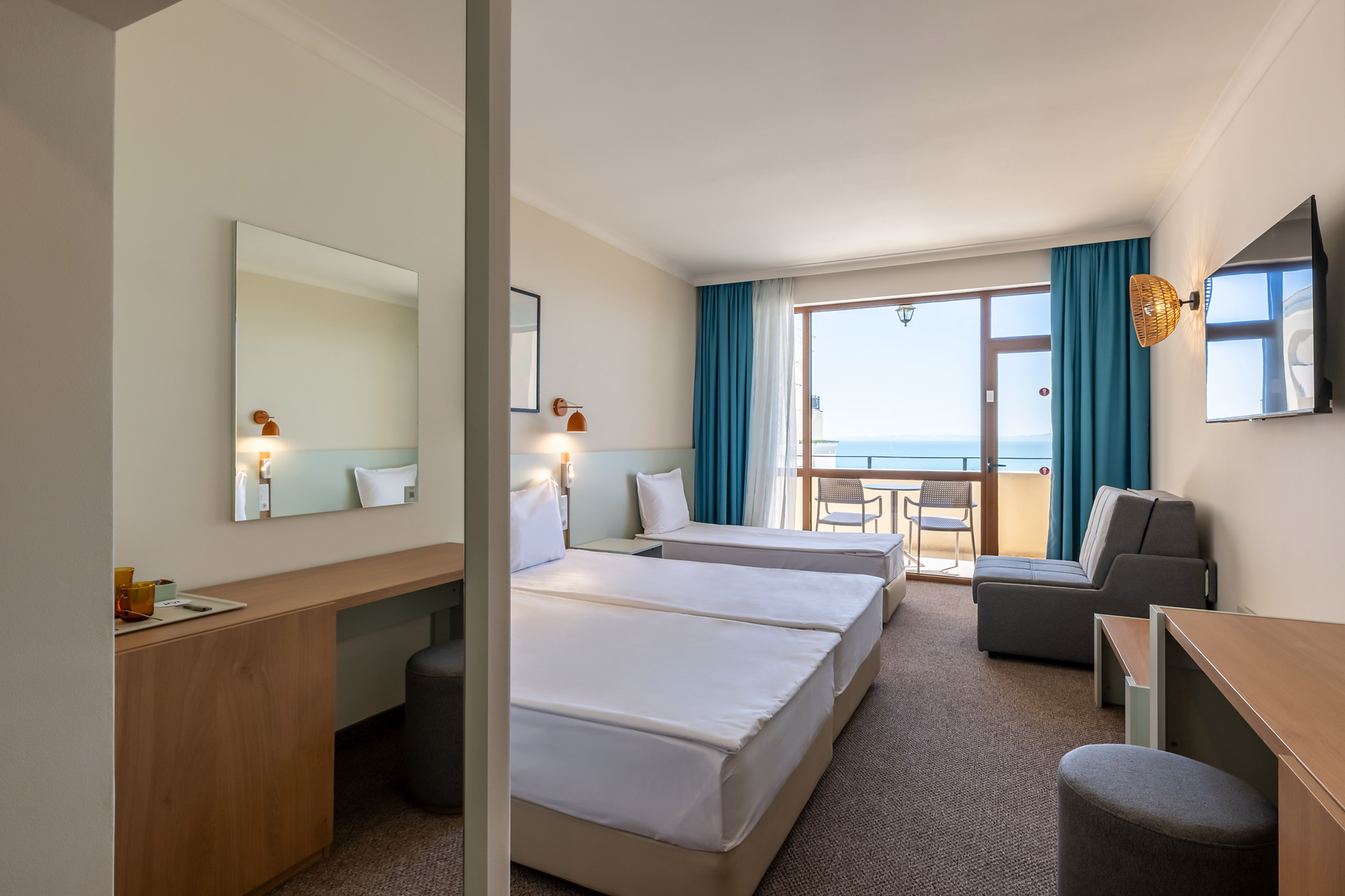 Hotel room with twin beds, desk, and balcony with ocean view.