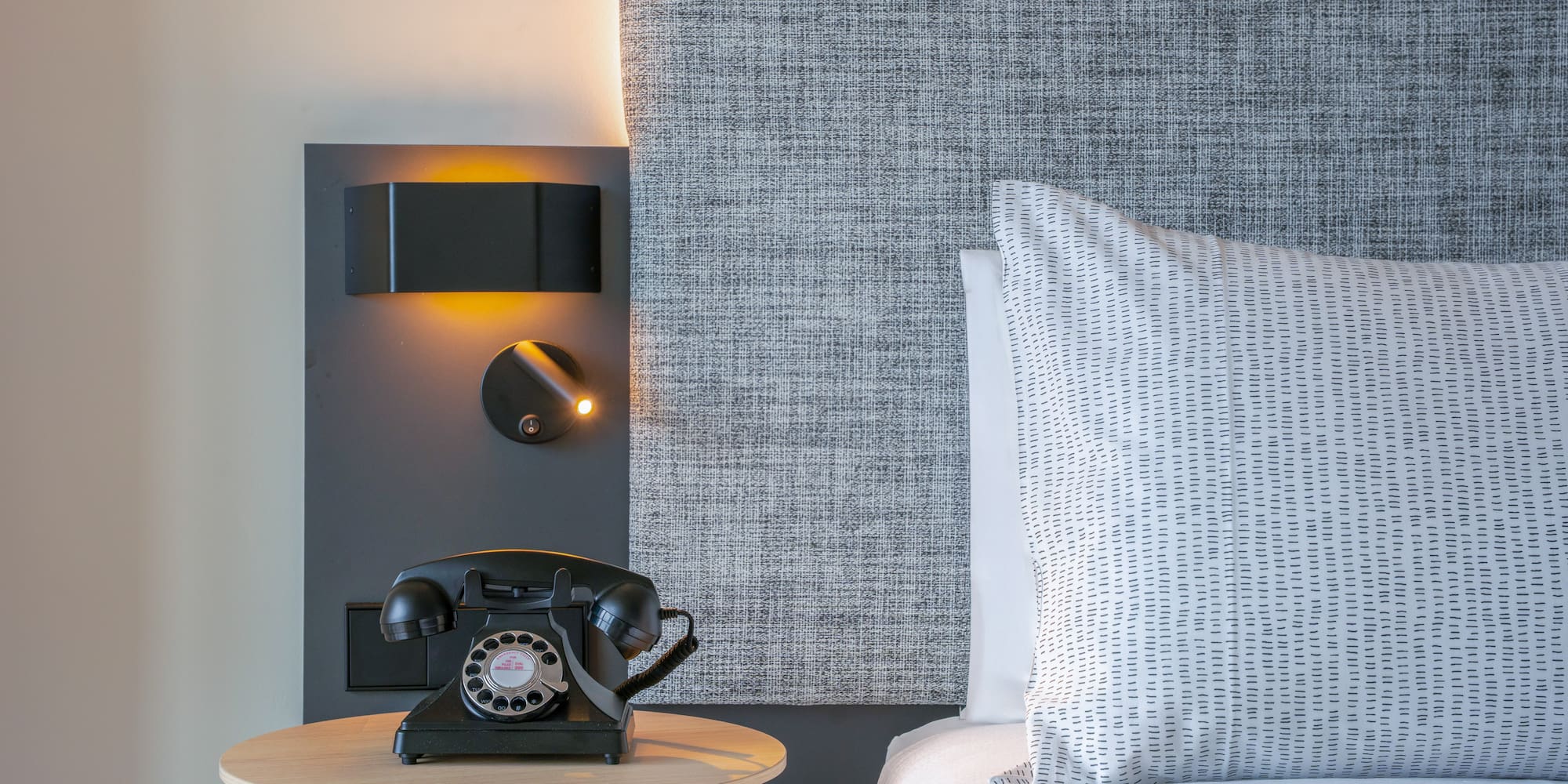 Habitación de hotel, mesita de noche, teléfono retro y cama con cabecero.