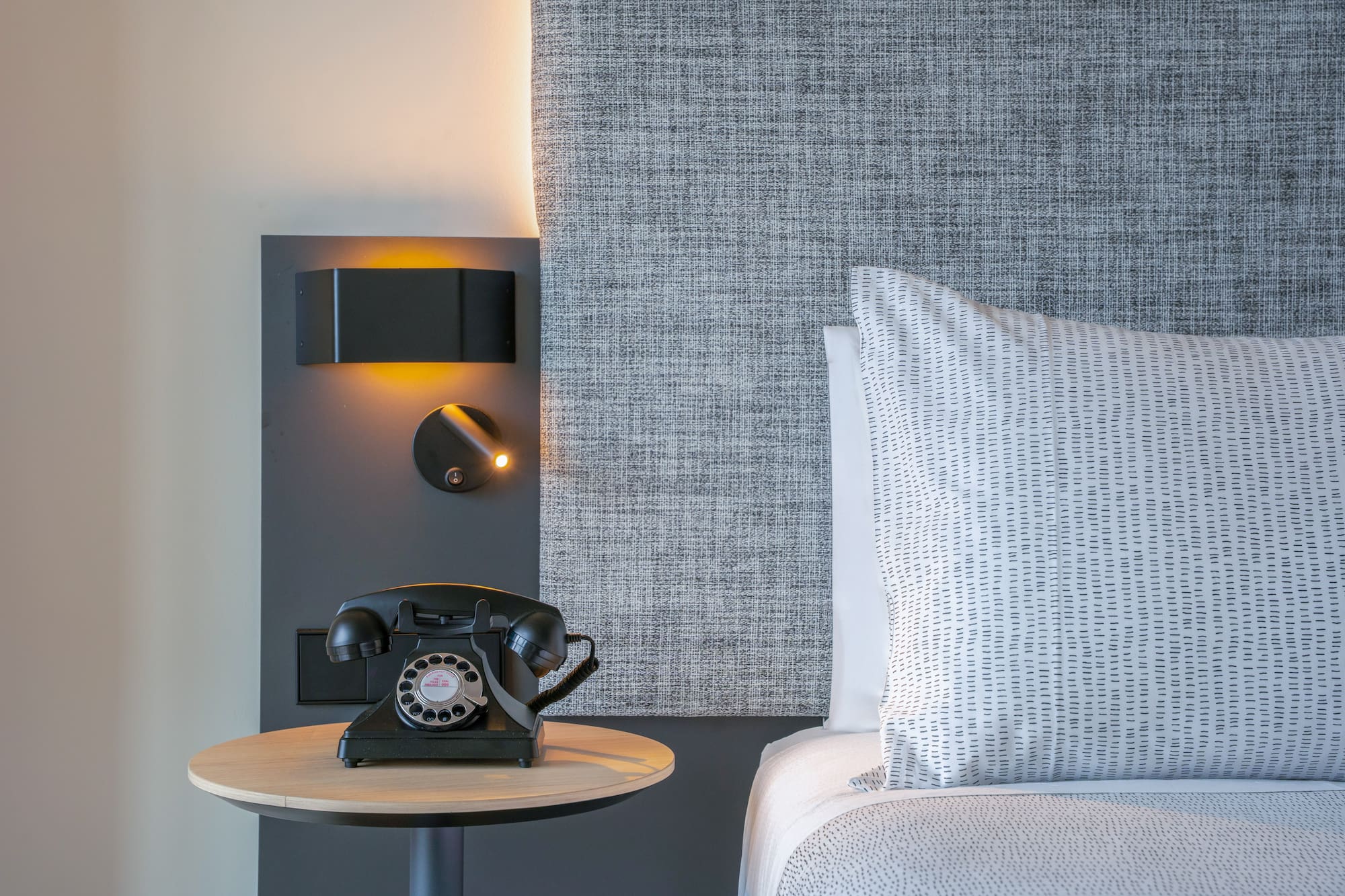 Habitación de hotel, mesita de noche, teléfono retro y cama con cabecero.