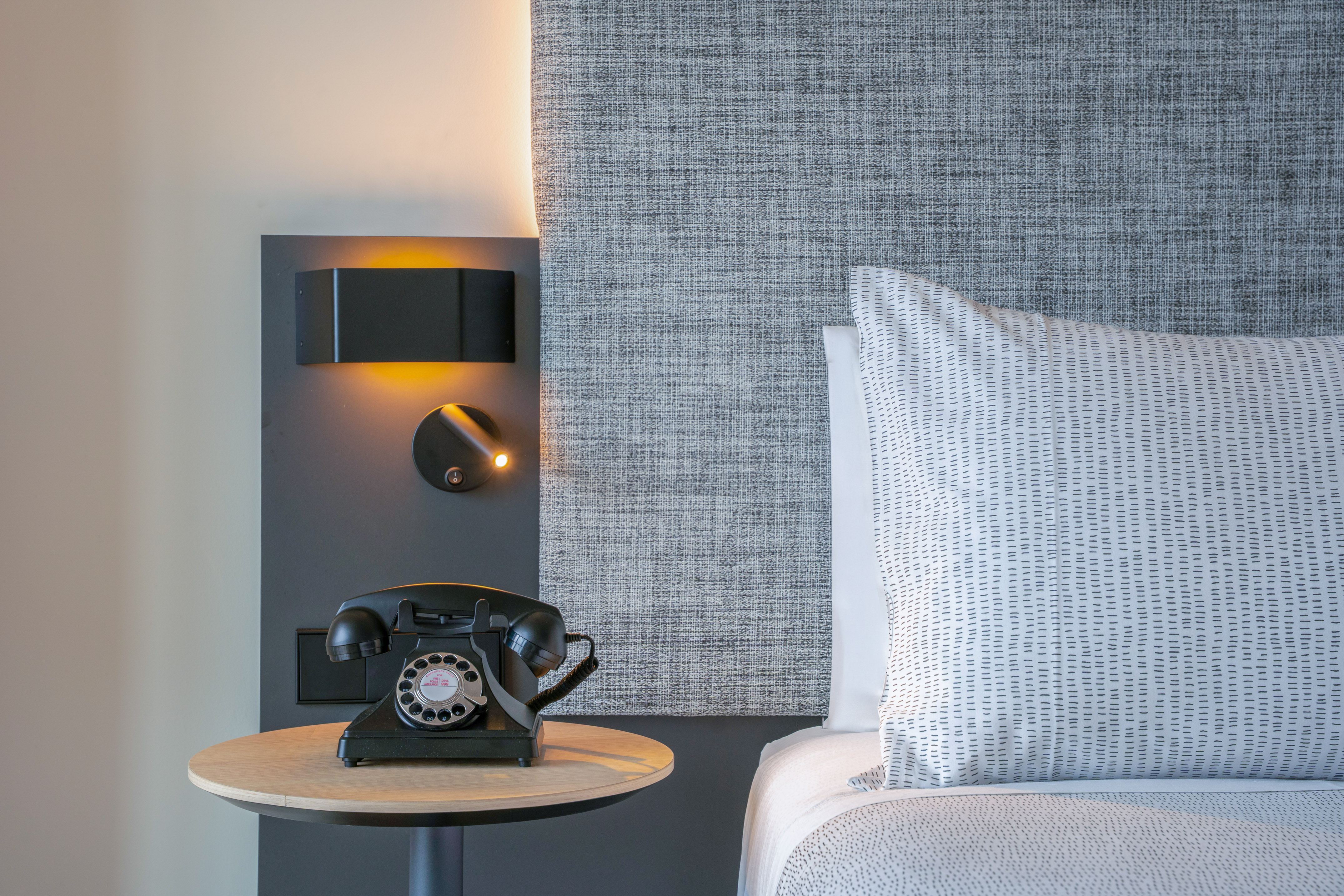 Habitación de hotel, mesita de noche, teléfono retro y cama con cabecero.