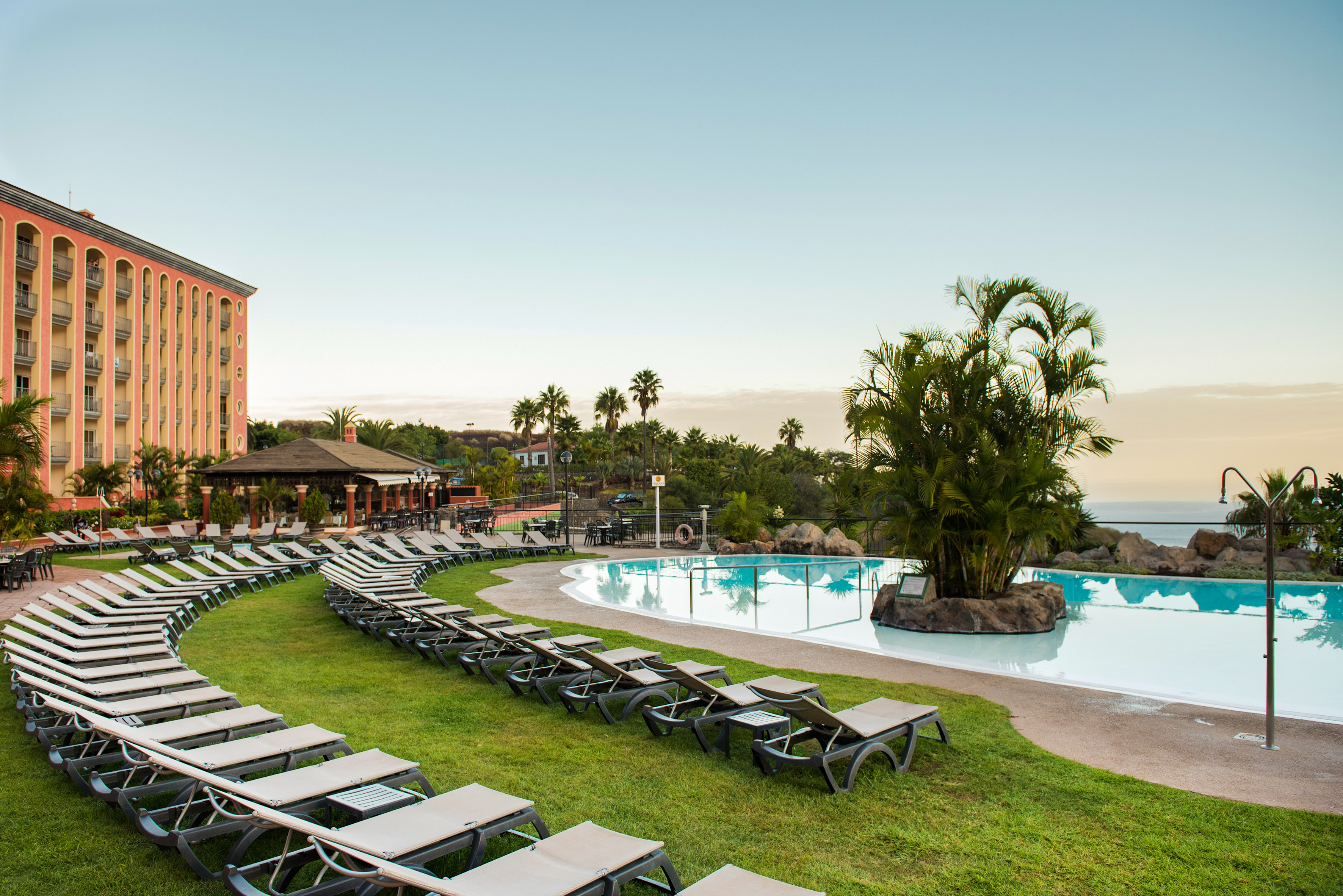 Tropical resort hotel with poolside lounge chairs, swimming pool, and palm trees.
