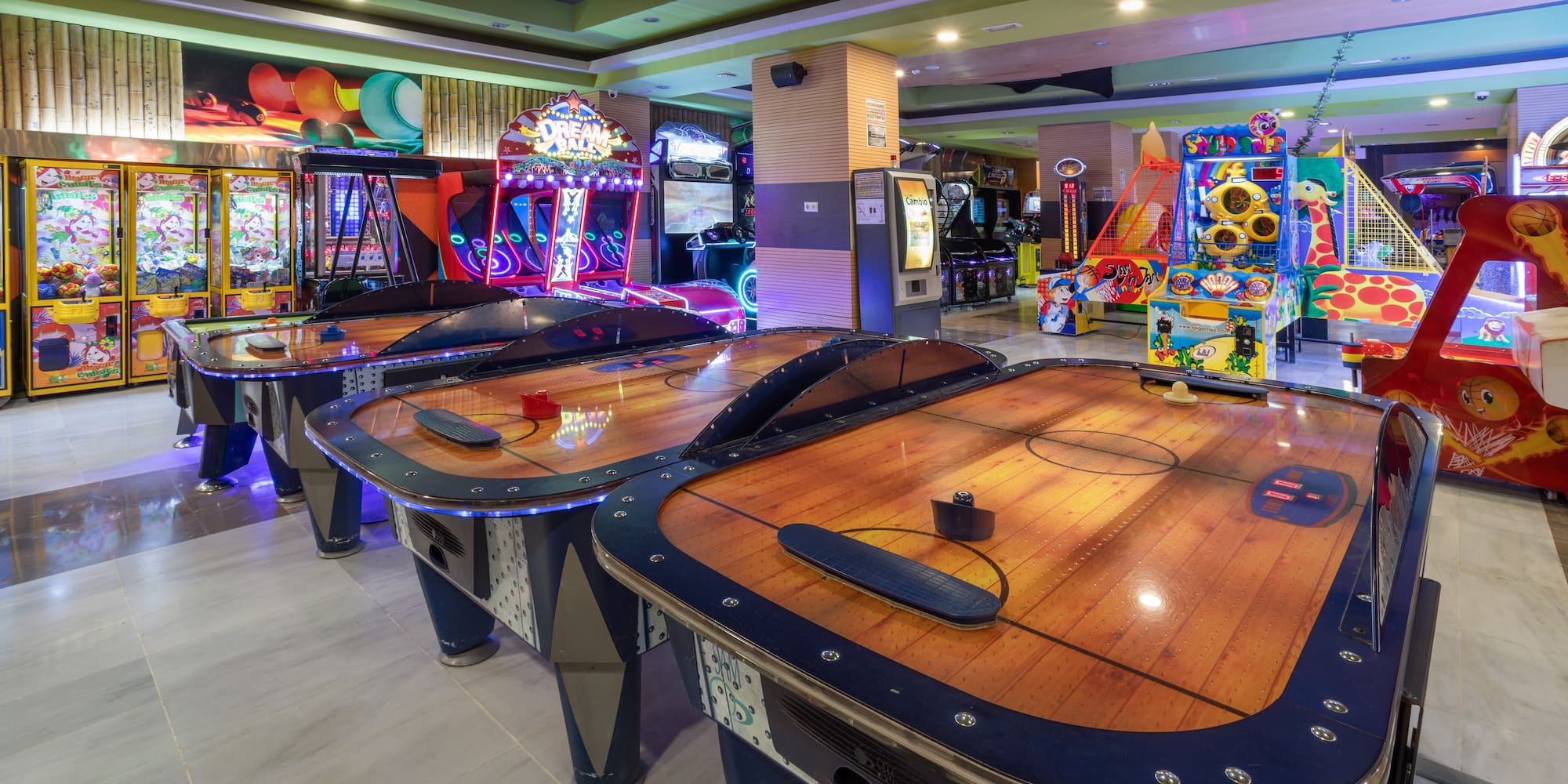 Bright arcade with air hockey tables, claw machines, and various games.