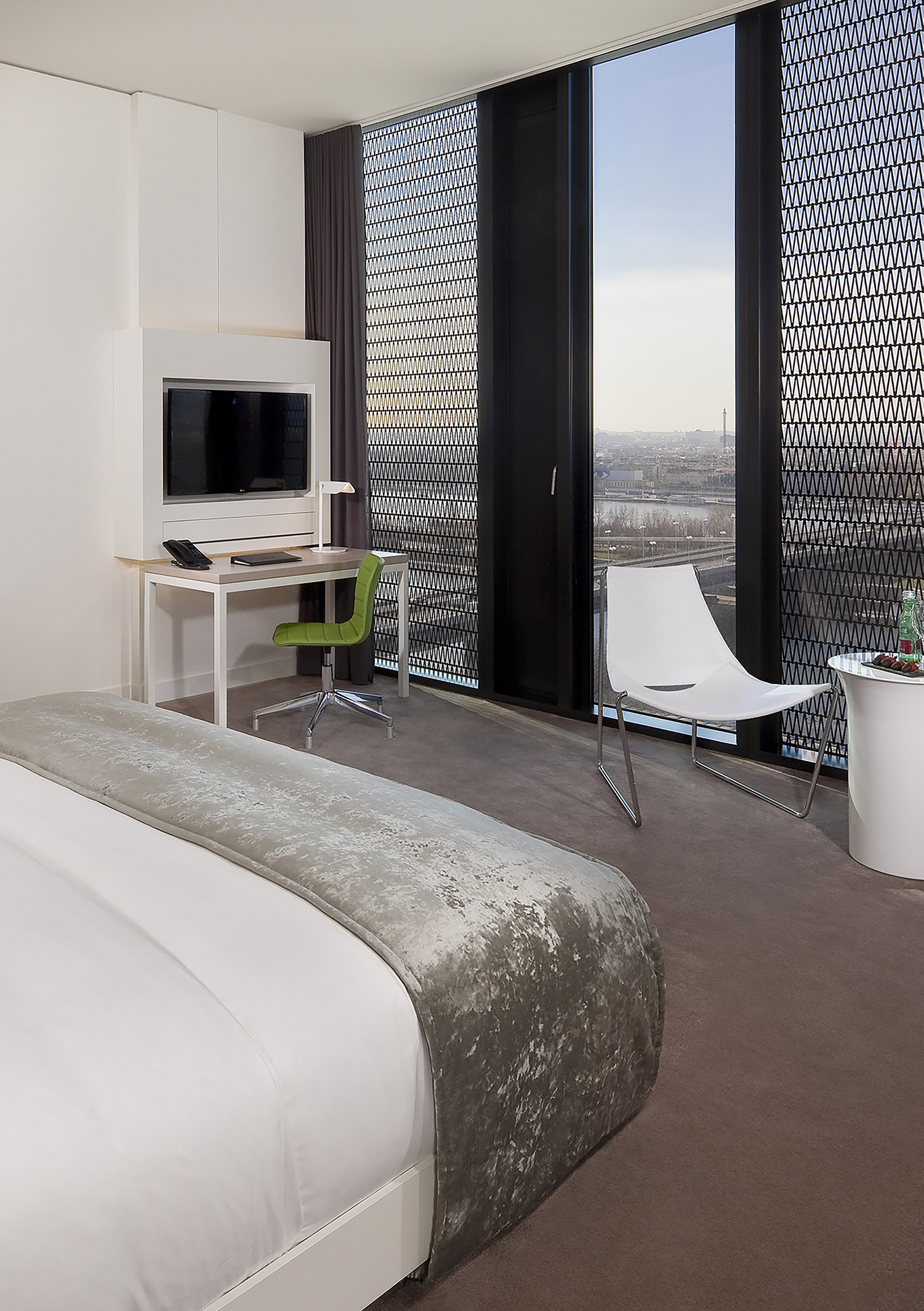 Contemporary hotel room with bed, desk, green chair, and city skyline view.