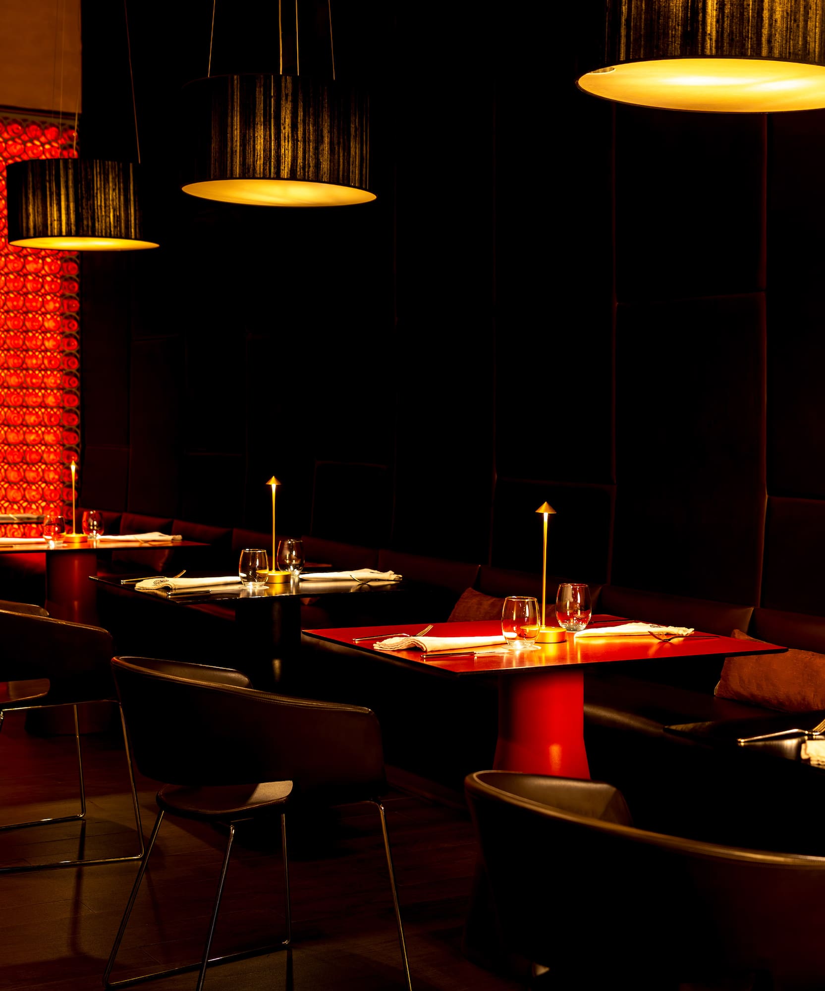 Dark modern restaurant dining room with warm lighting and a red textured wall.
