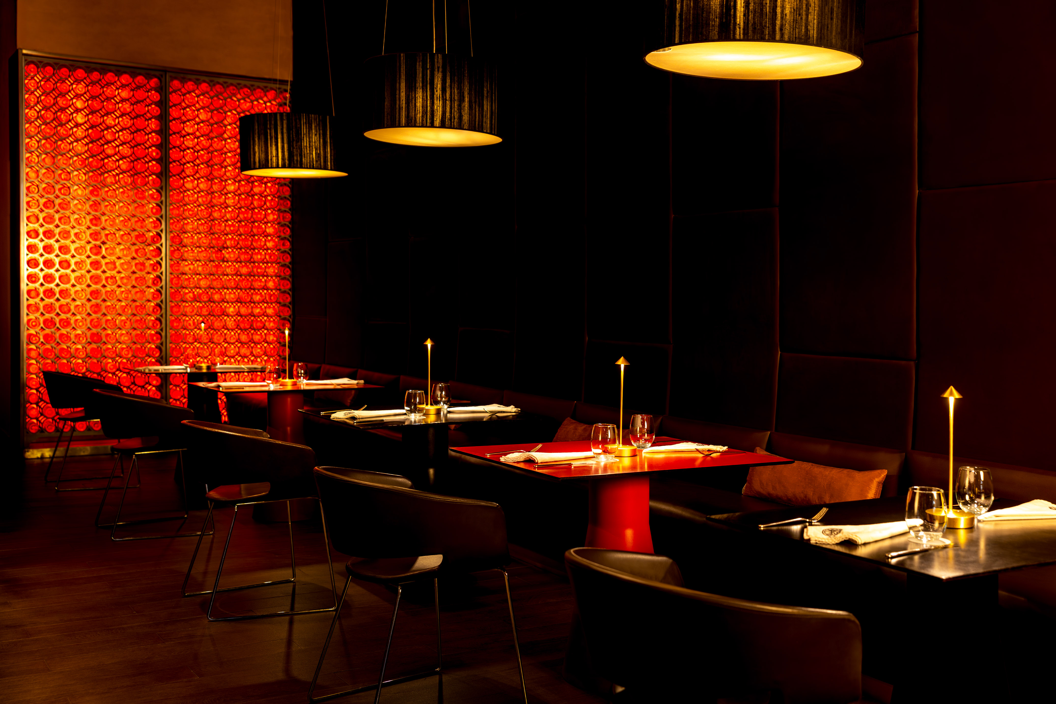 Dark modern restaurant dining room with warm lighting and a red textured wall.