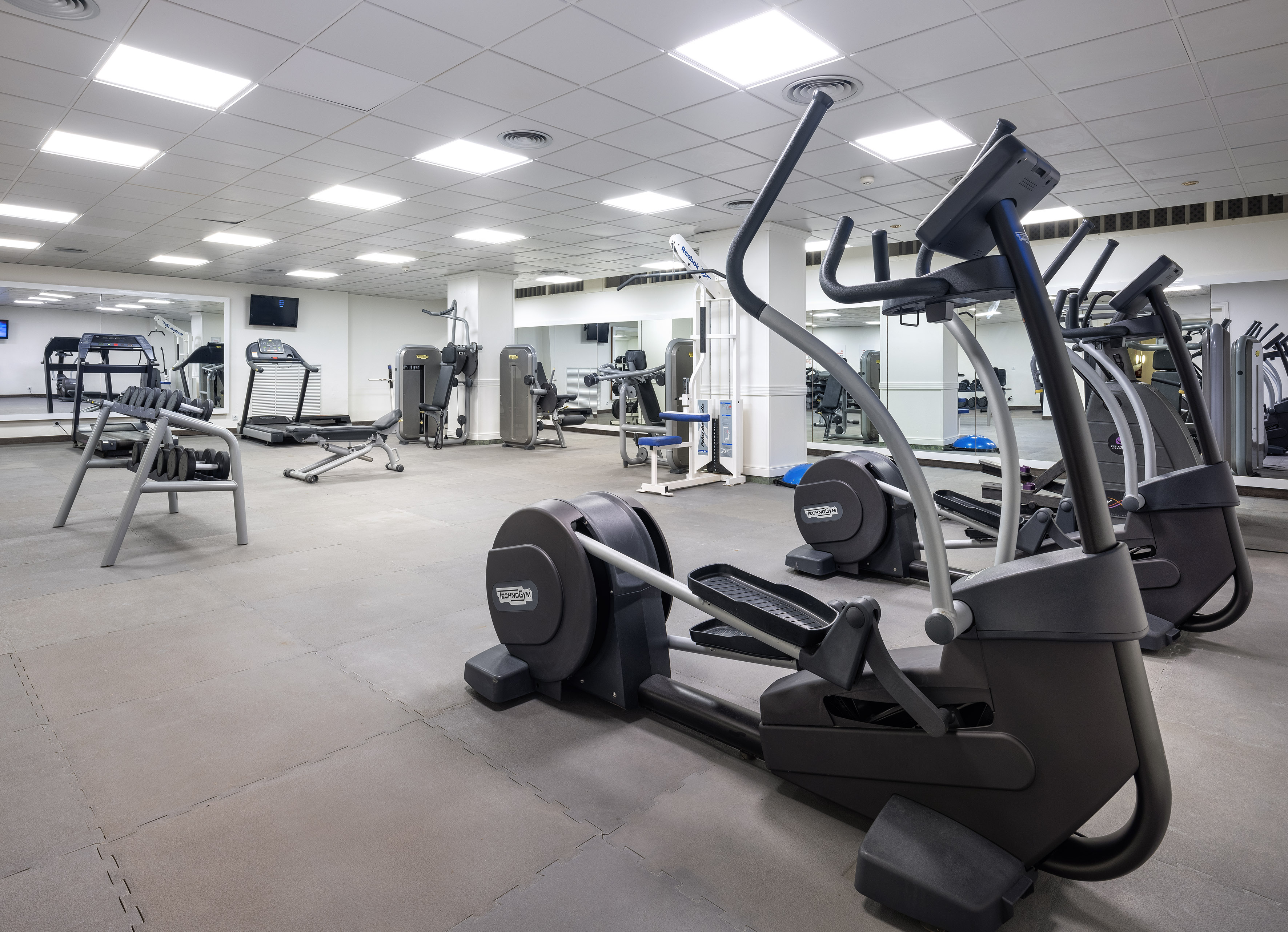 Well-equipped gym with ellipticals, treadmills, weight machines, and dumbbells.