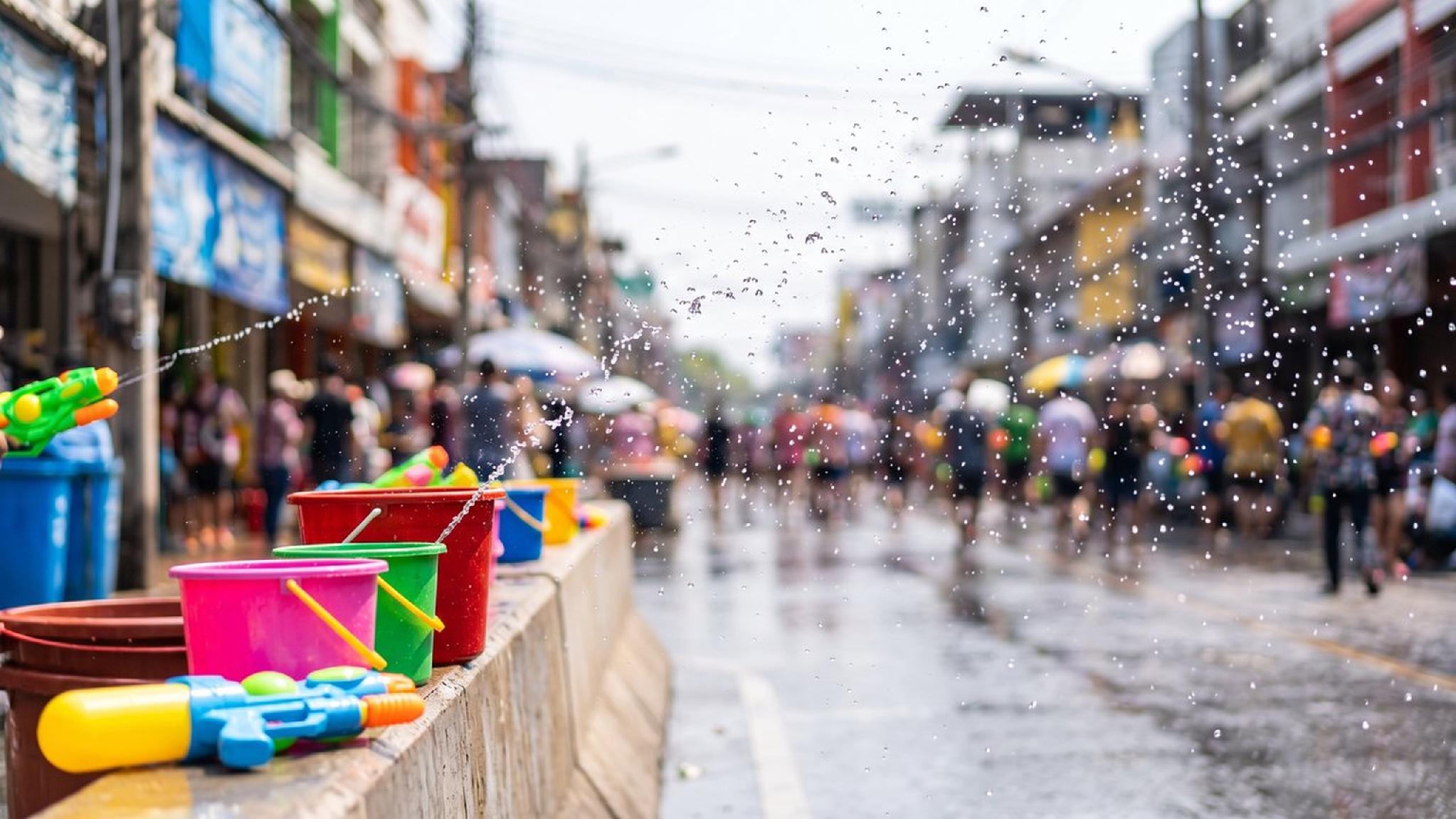 Colorful water guns and buckets on a wet street during Songkran festival.