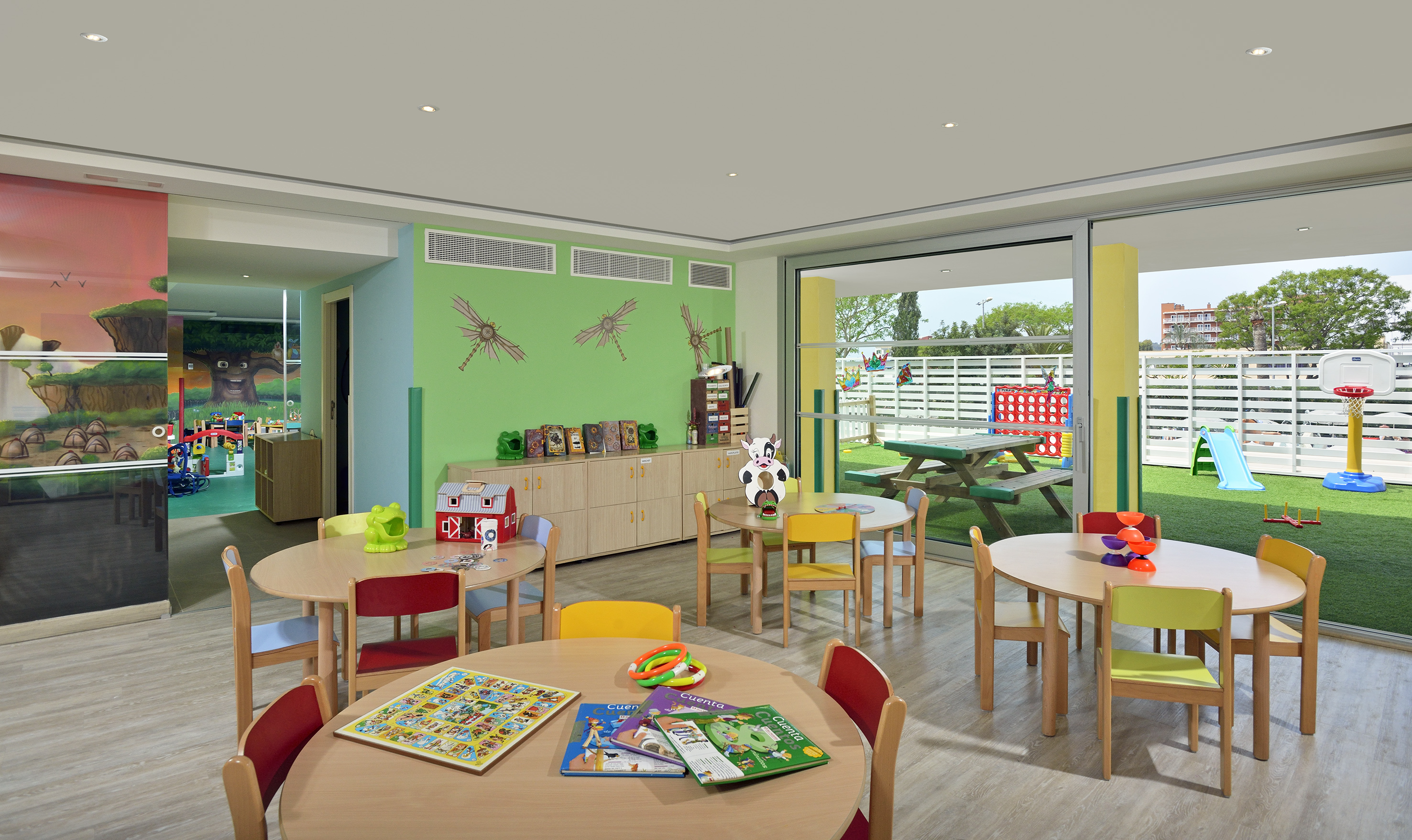 Colorful kids' playroom with tables, toys, and sunny outdoor playground activities.