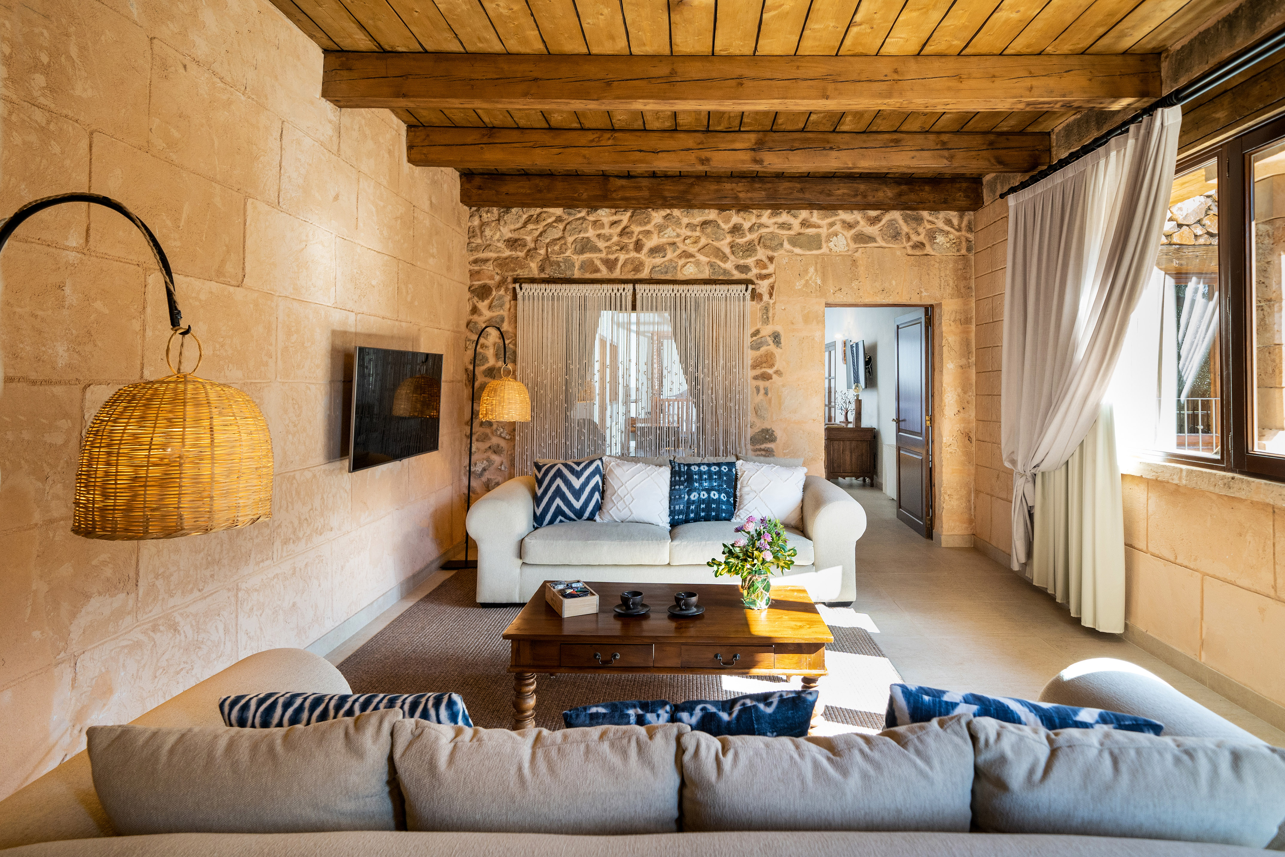 Rustic living room with stone walls, wooden beams, white sofa, and coffee table.
