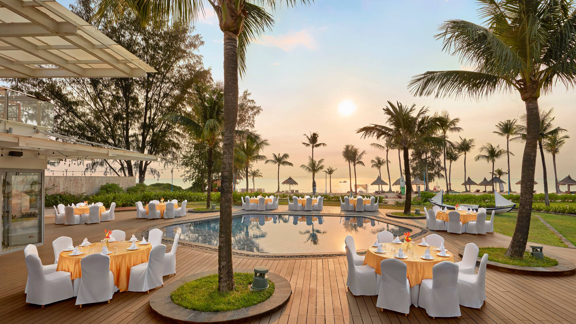 Elegant outdoor poolside dining at a tropical resort with sunset ocean view.