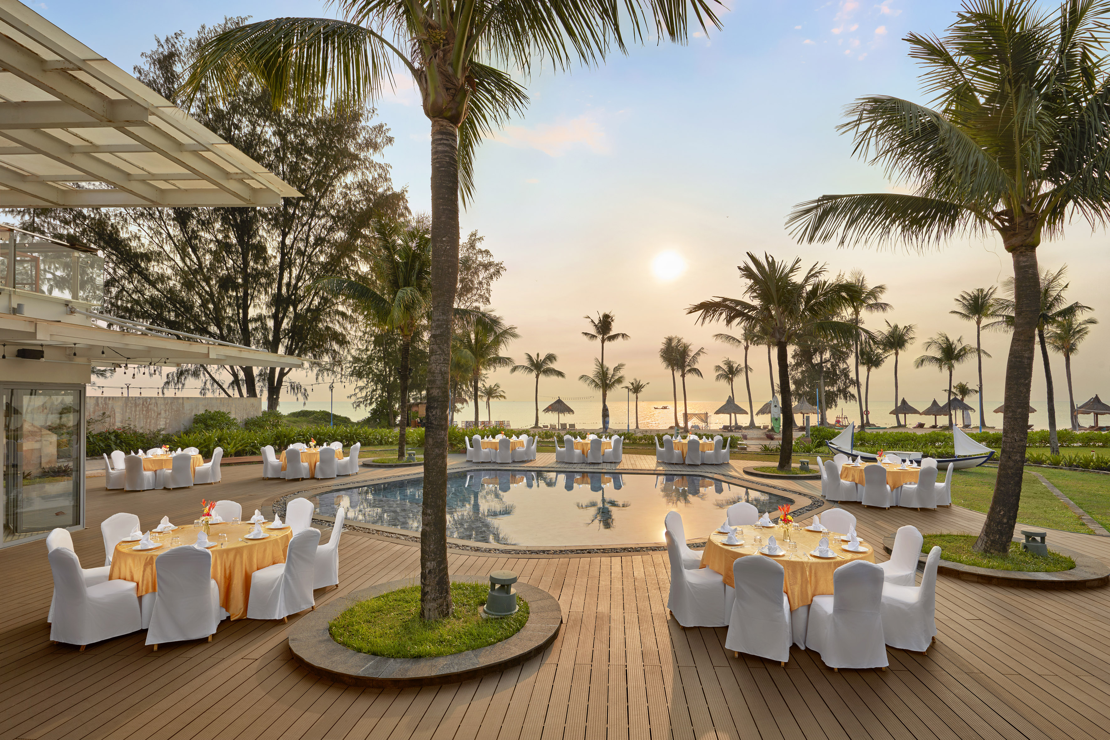 Elegant outdoor poolside dining at a tropical resort with sunset ocean view.