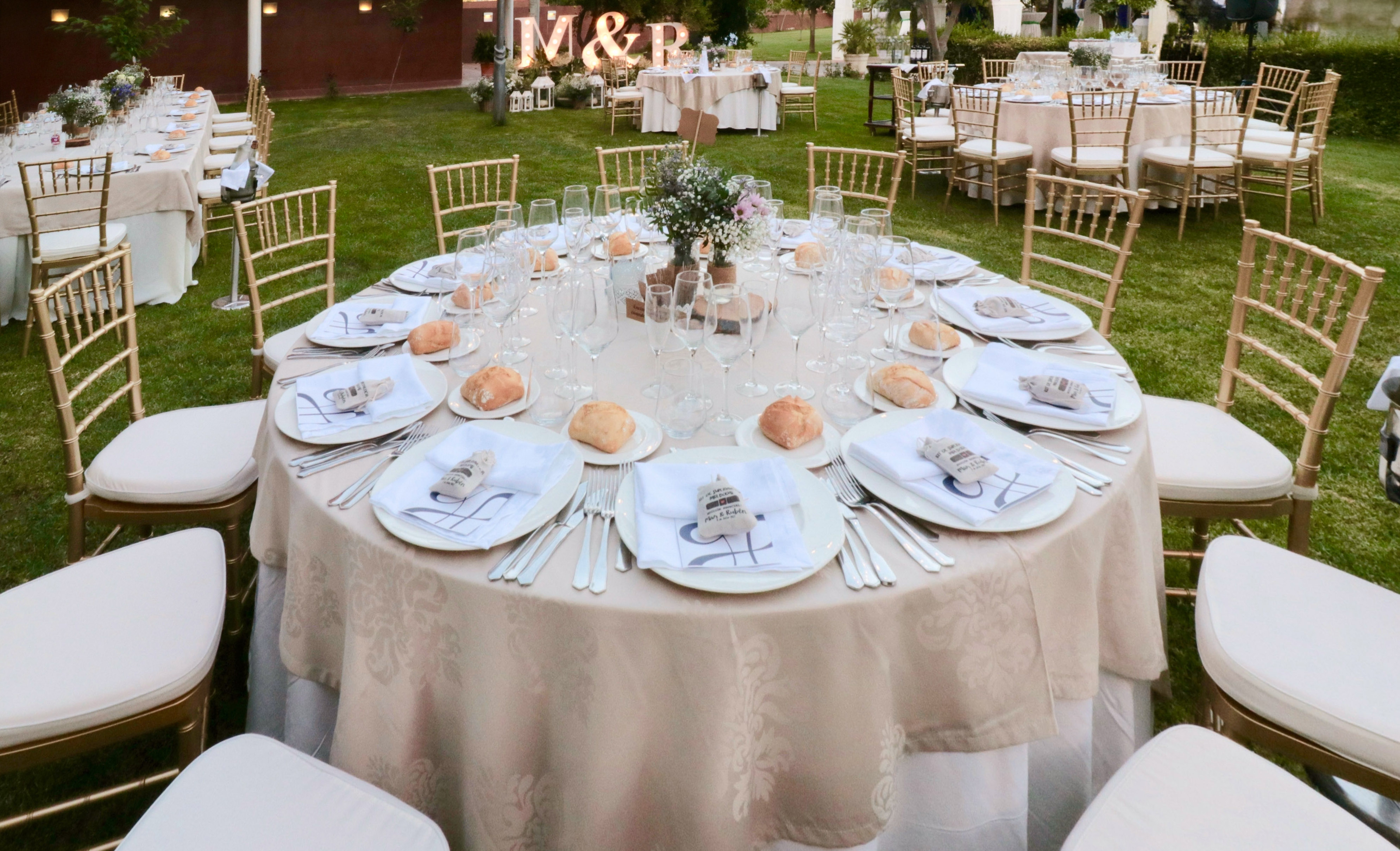 Elegant outdoor wedding reception table setting with gold chairs and floral centerpiece.