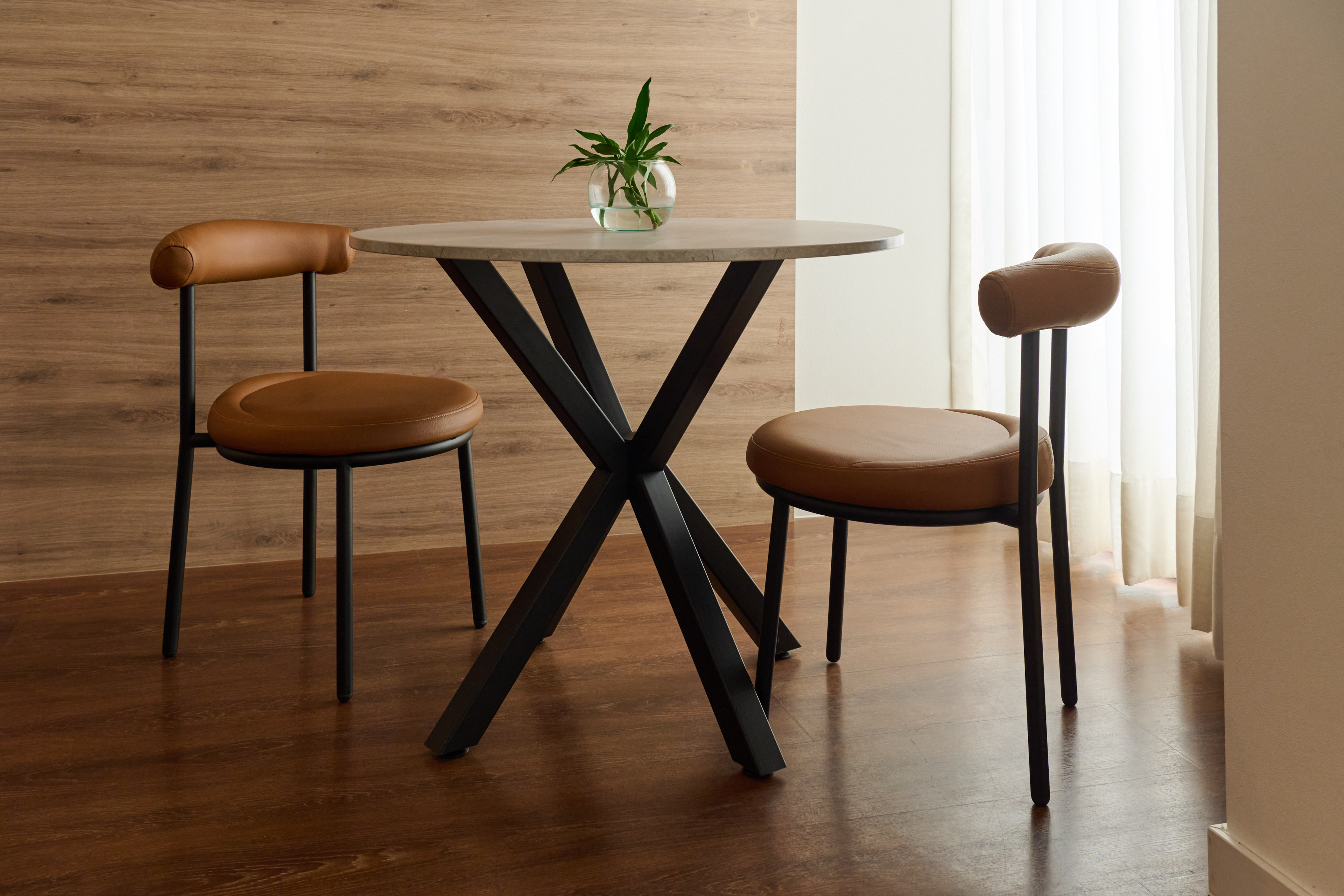 Modern dining set: round table, black base, two brown leather chairs.