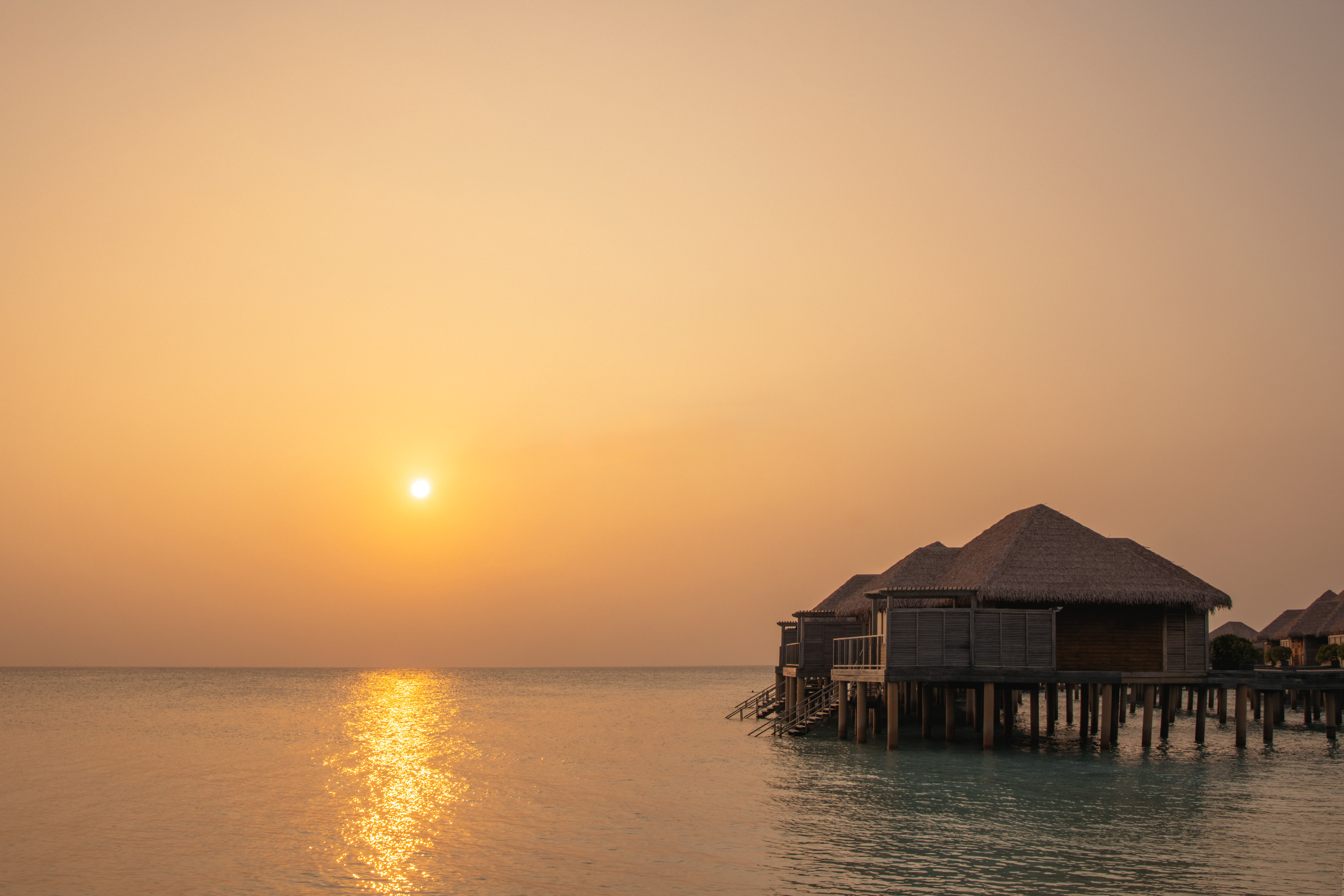 Tropical overwater bungalows on calm ocean at golden sunset.