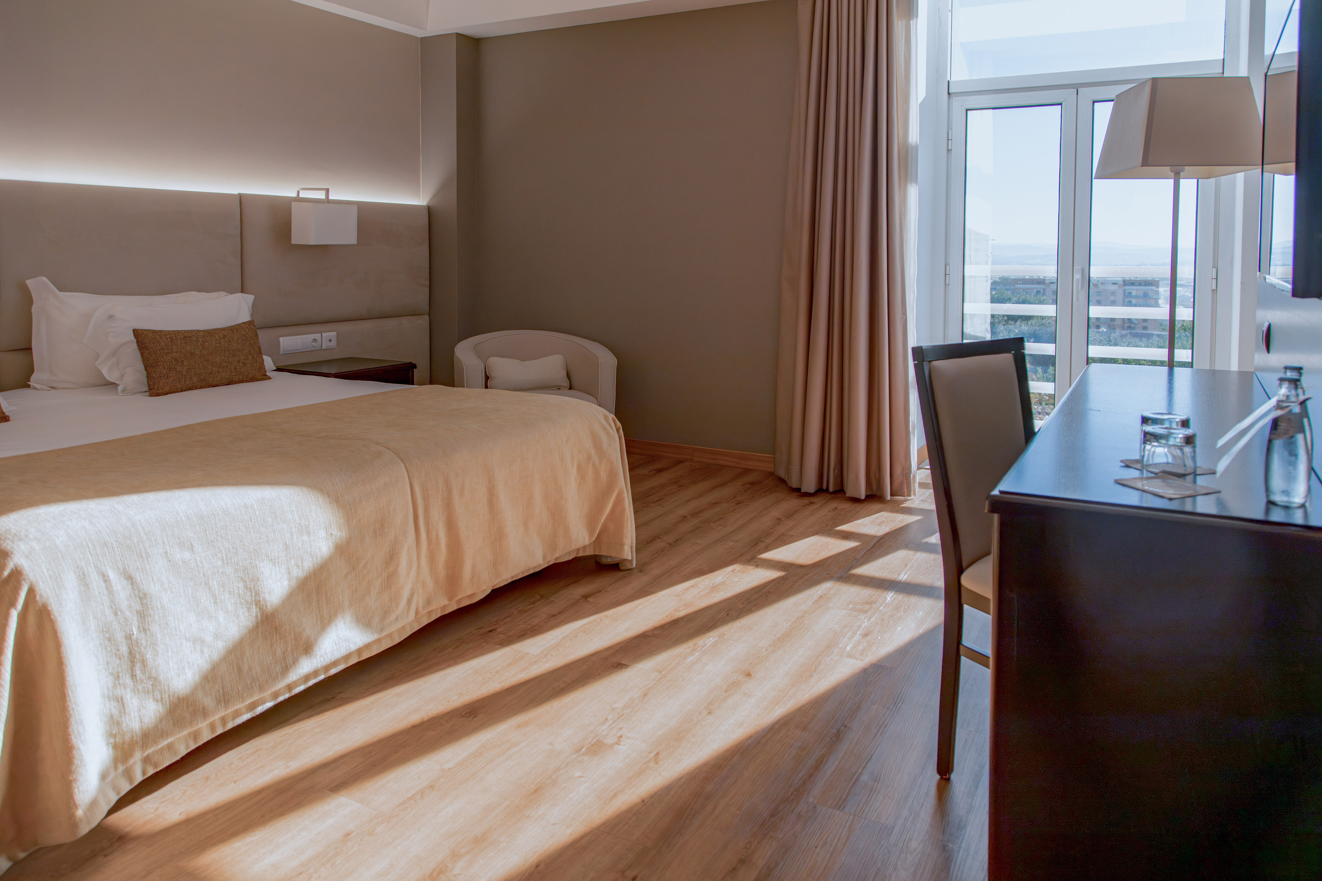 Hotel room with comfortable bed, wood floor, bright window, and desk area.