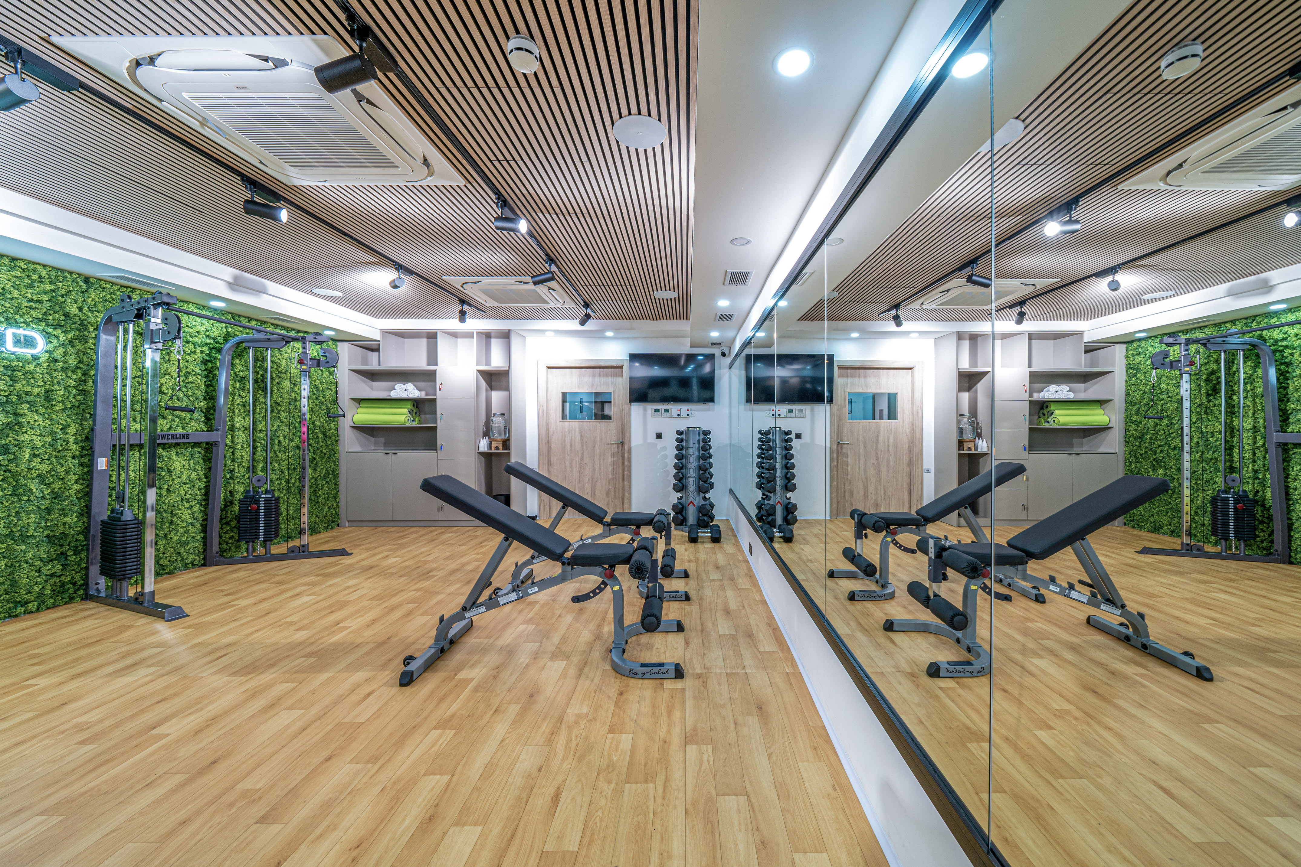Modern gym with green moss wall, wood floor, weight benches, and cable machines.