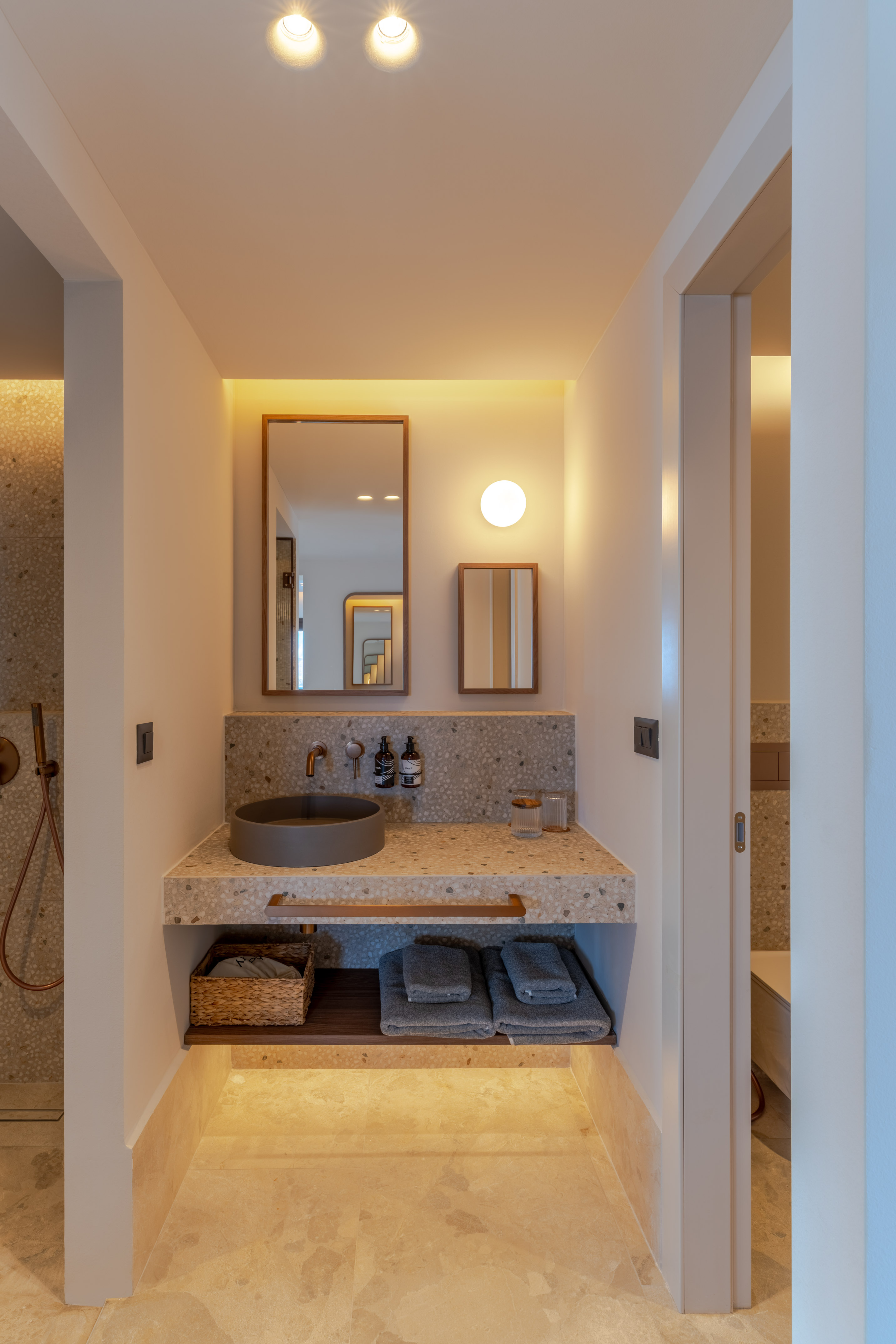 Modern bathroom vanity with terrazzo counter, gray sink, copper faucet, mirrors.