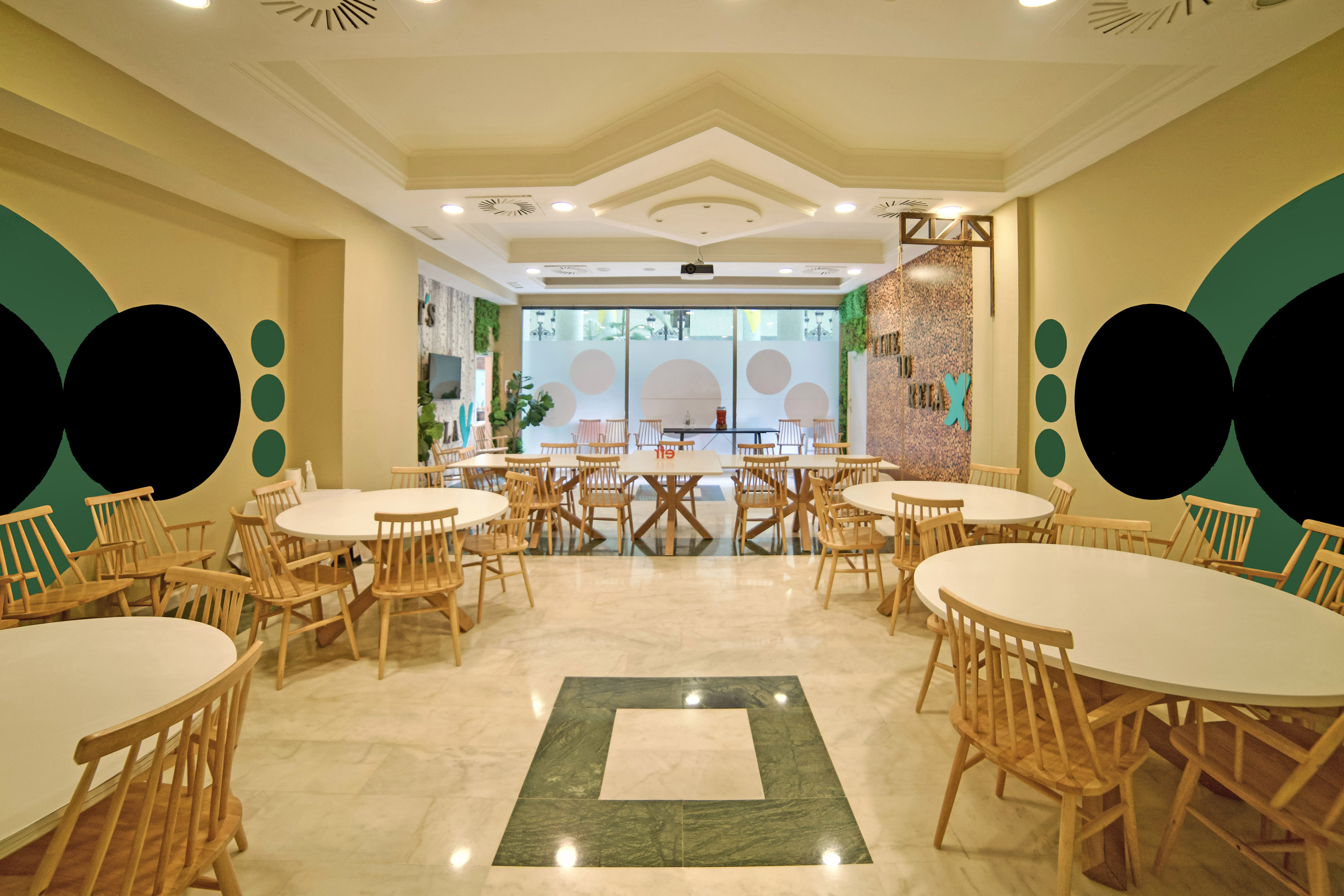Modern restaurant dining area with white tables, wooden chairs, green accents.