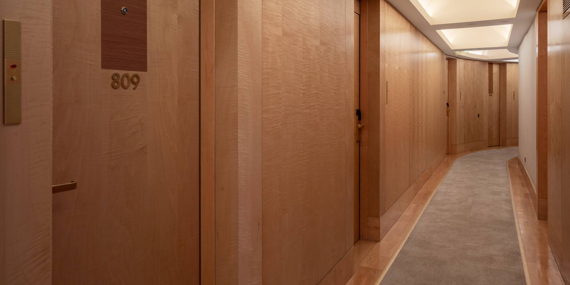 Modern hotel hallway with light wood paneling, illuminated ceiling, and room 809.